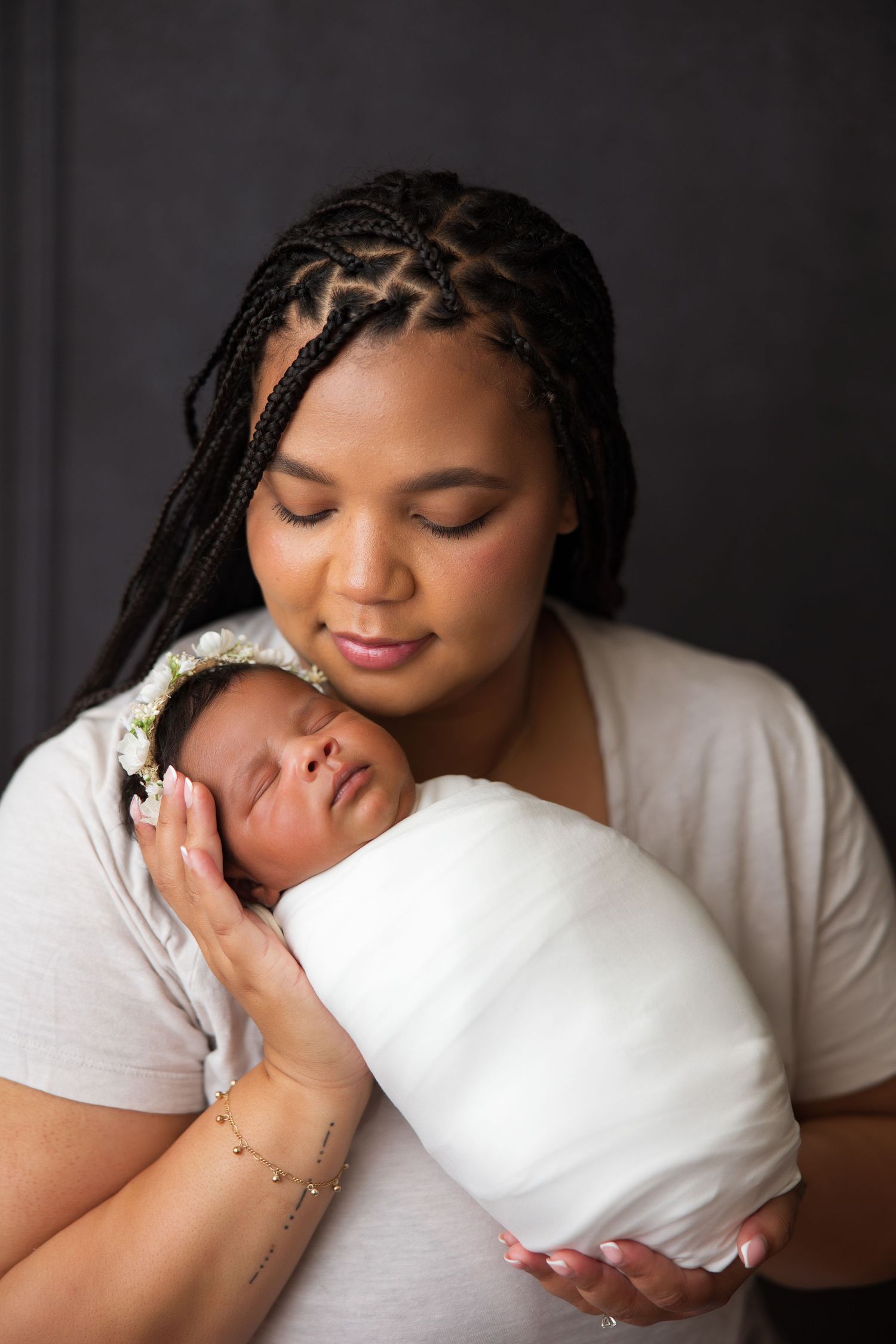 Tender moment with sleeping newborn wrapped in white swaddle against dark background.