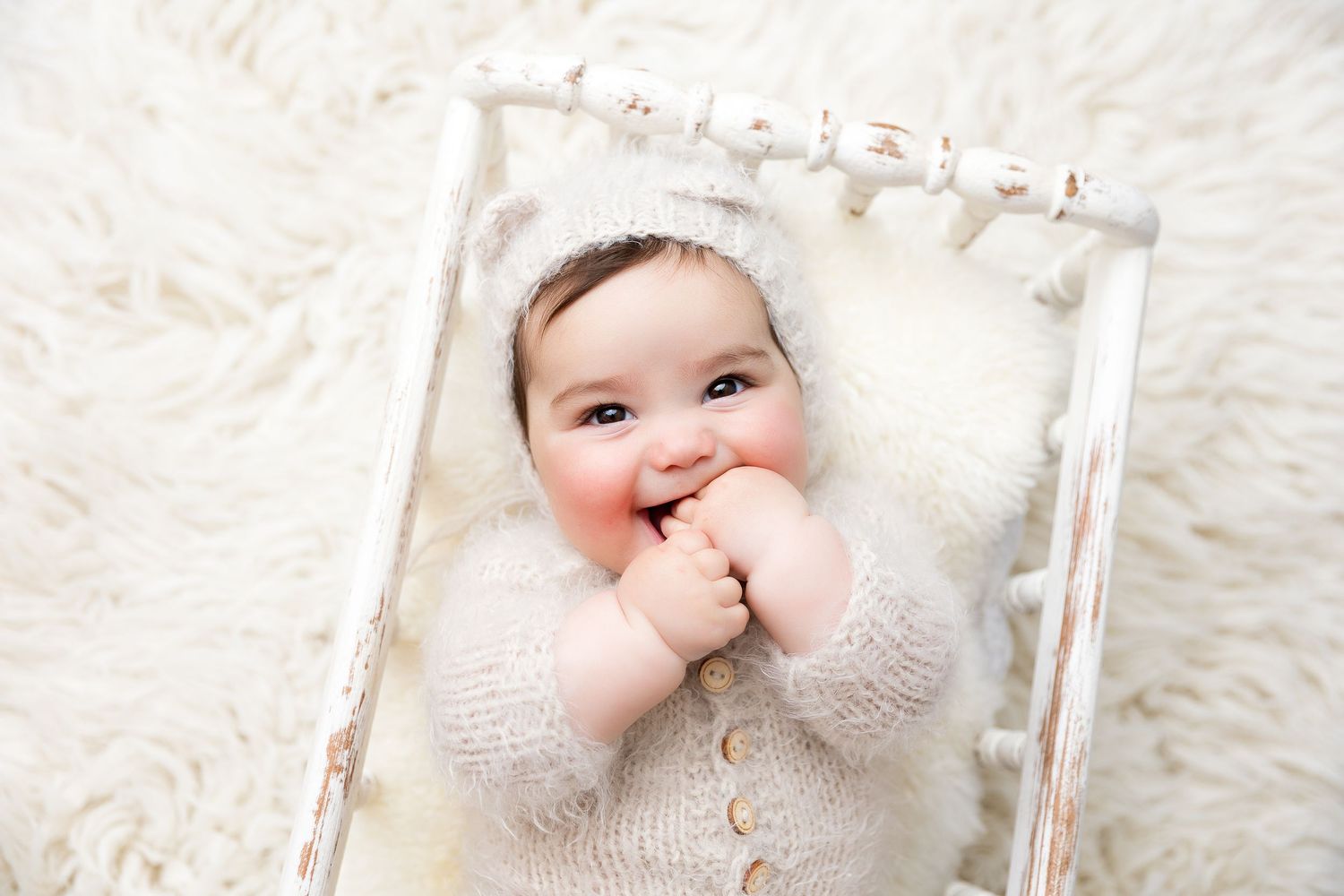 Baby in cozy knit outfit lying on plush white rug.