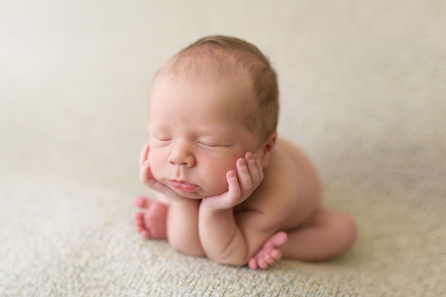 Newborn peacefully resting on cream colored carpet in natural pose.