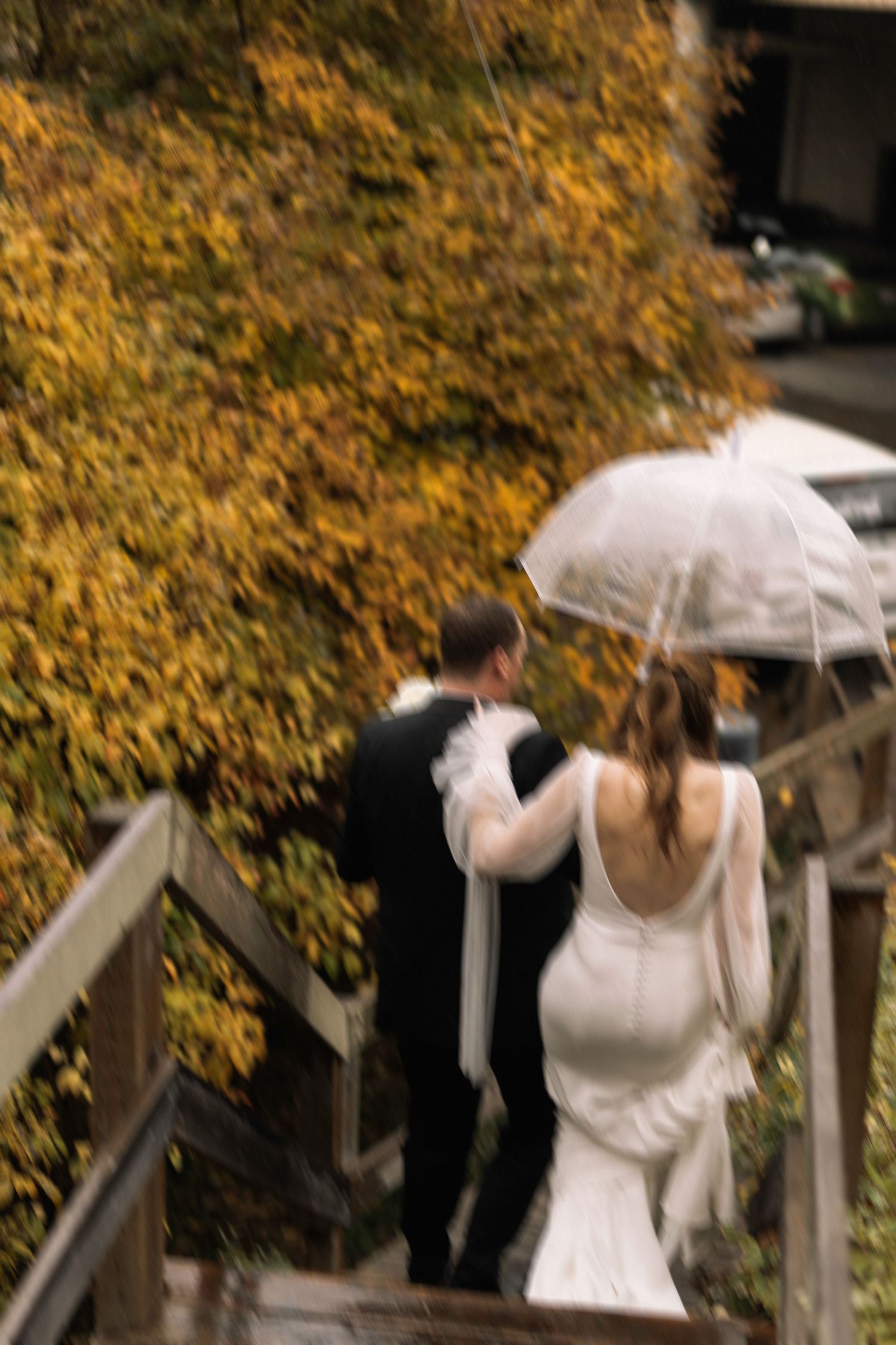 Couple walking down stairs with white umbrella against autumn foliage backdrop.