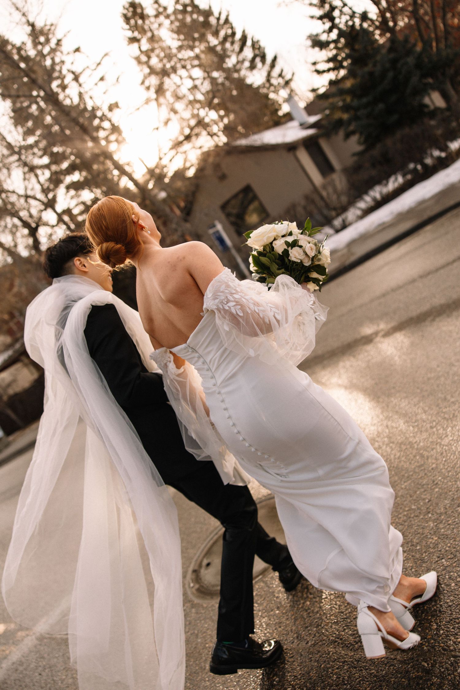 A romantic dip kiss between newlyweds outdoors at sunset with flowing white wedding dress and veil.