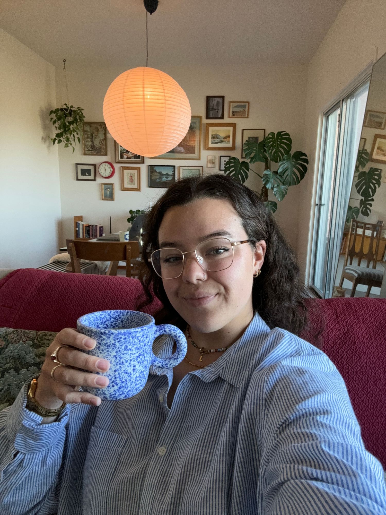 Person in striped shirt holding blue speckled ceramic mug in living room.