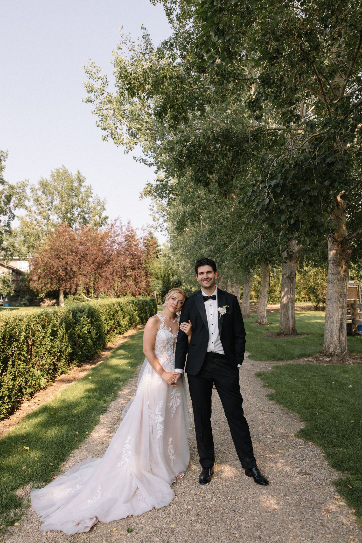 Bride and groom posing on a garden path surrounded by lush trees on their wedding day.