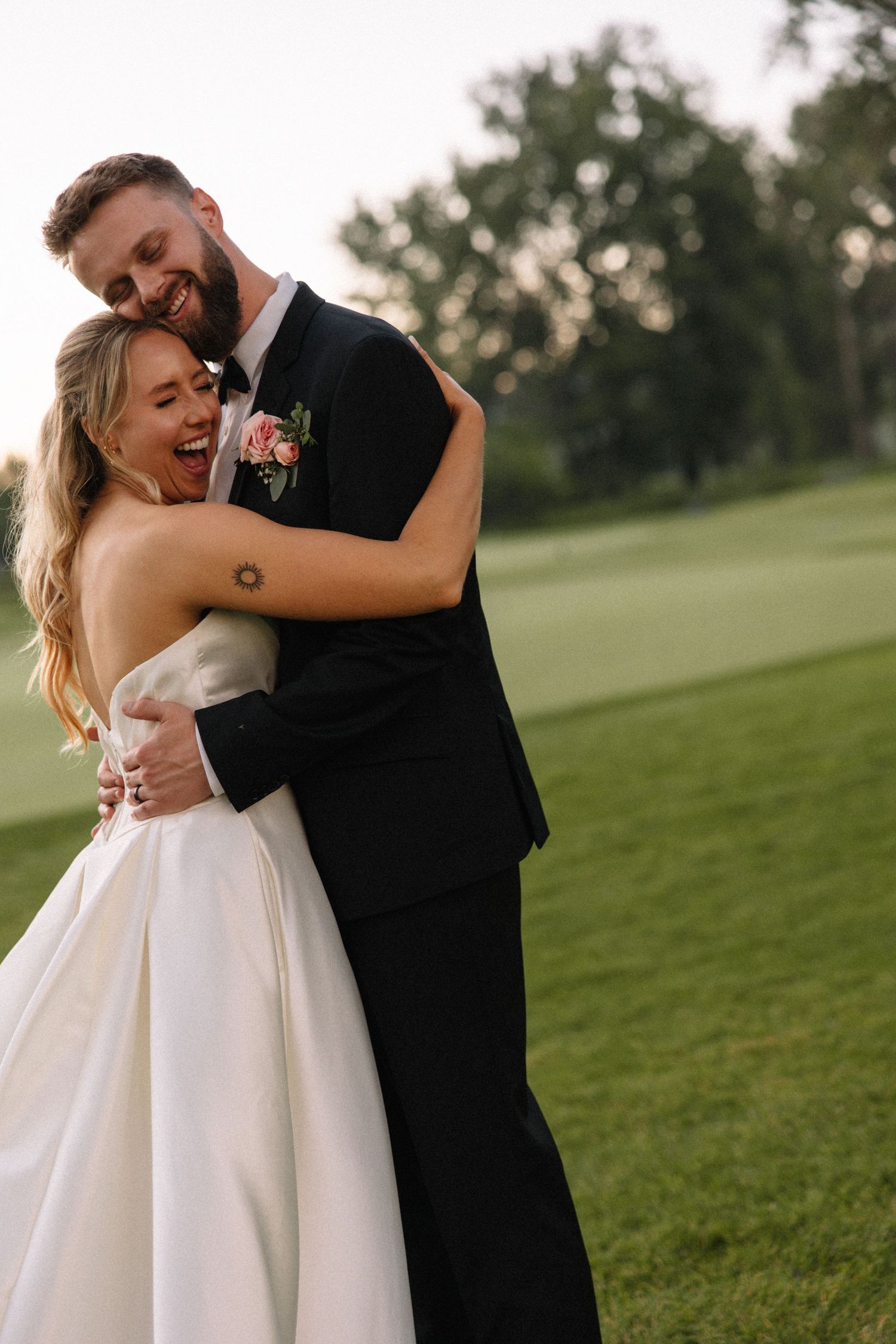 Joyful wedding couple embracing and laughing together on a green lawn.