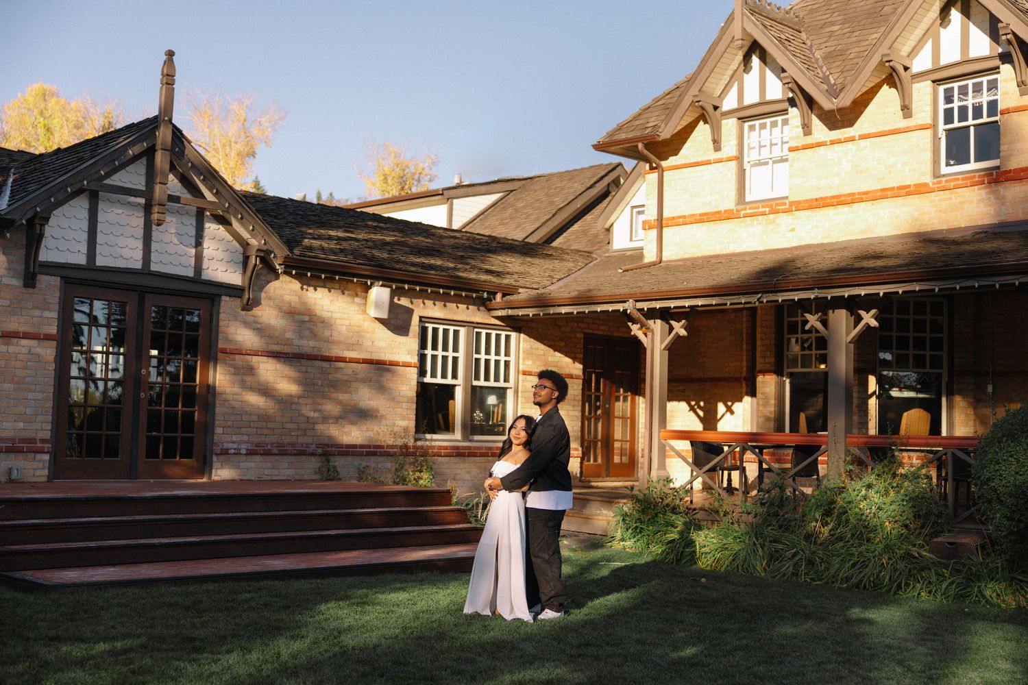 Couple stands outside Tudor-style venue during golden hour wedding photography session.
