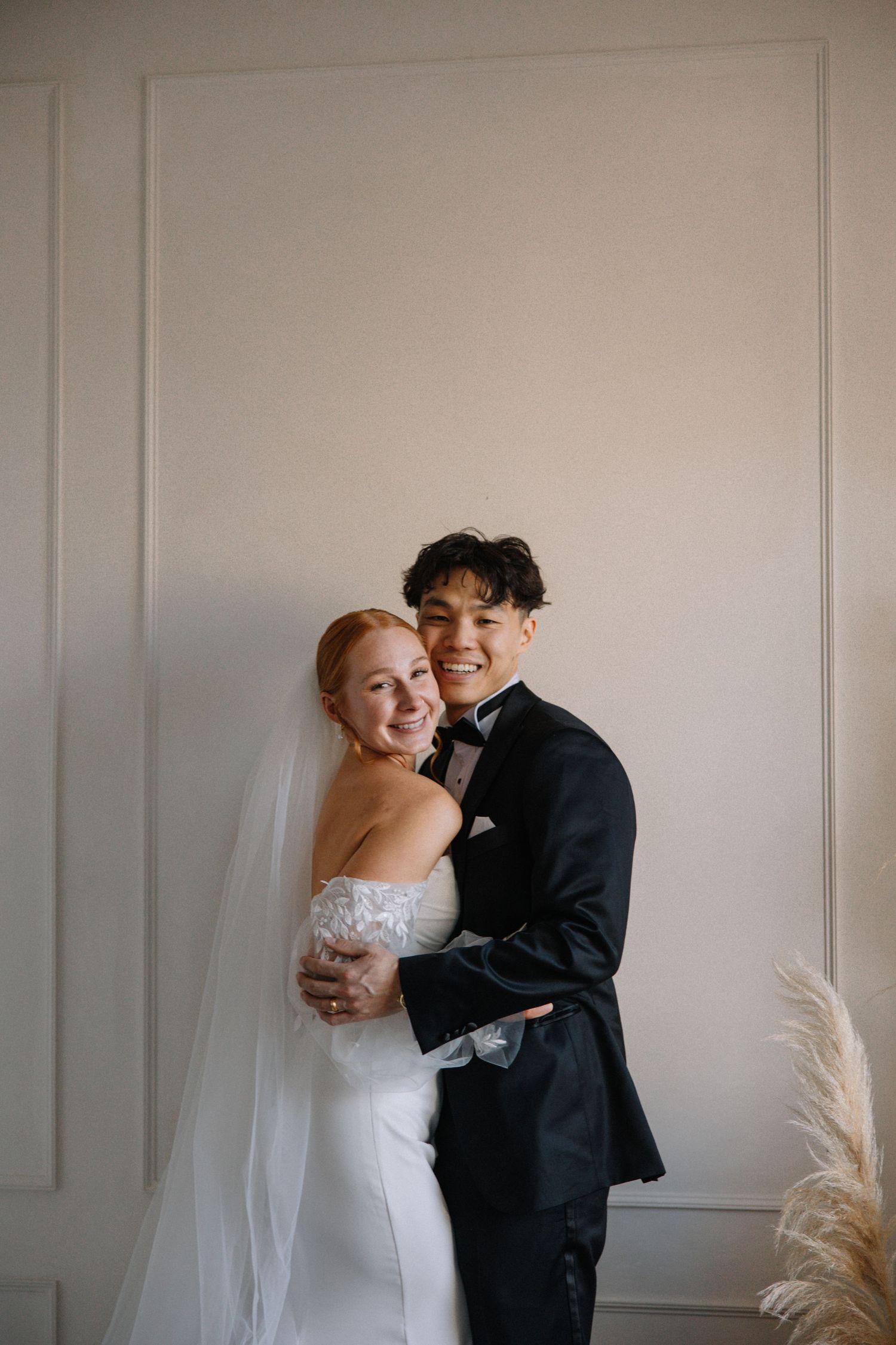 Intimate portrait of newlyweds embracing against a minimalist white wall.