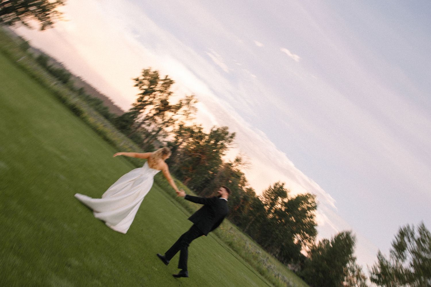A person in a wedding dress spins gracefully on a lush green lawn during sunset, creating a flowing motion effect.