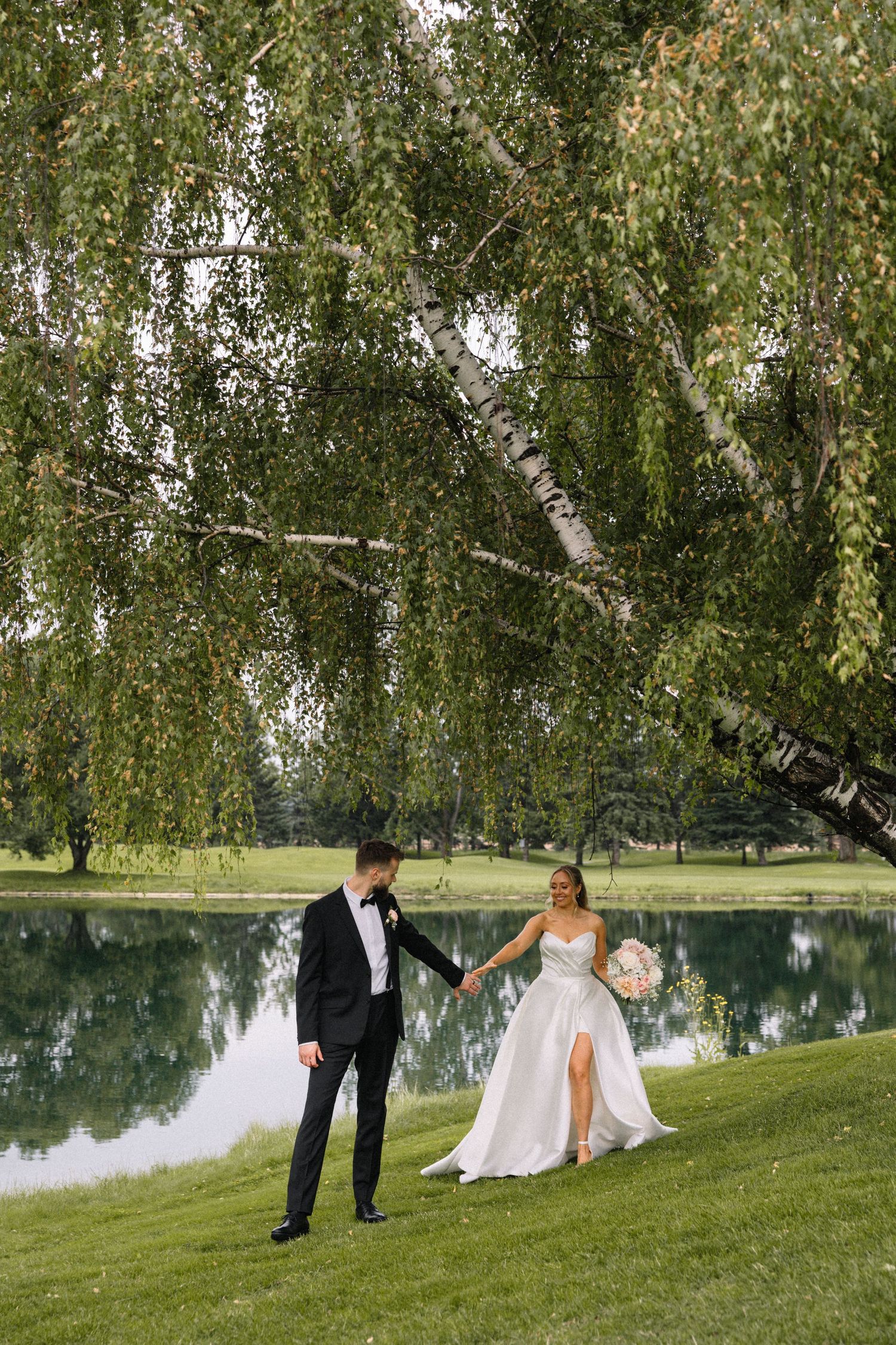 Wedding couple poses for romantic photos by a serene lake surrounded by birch trees.