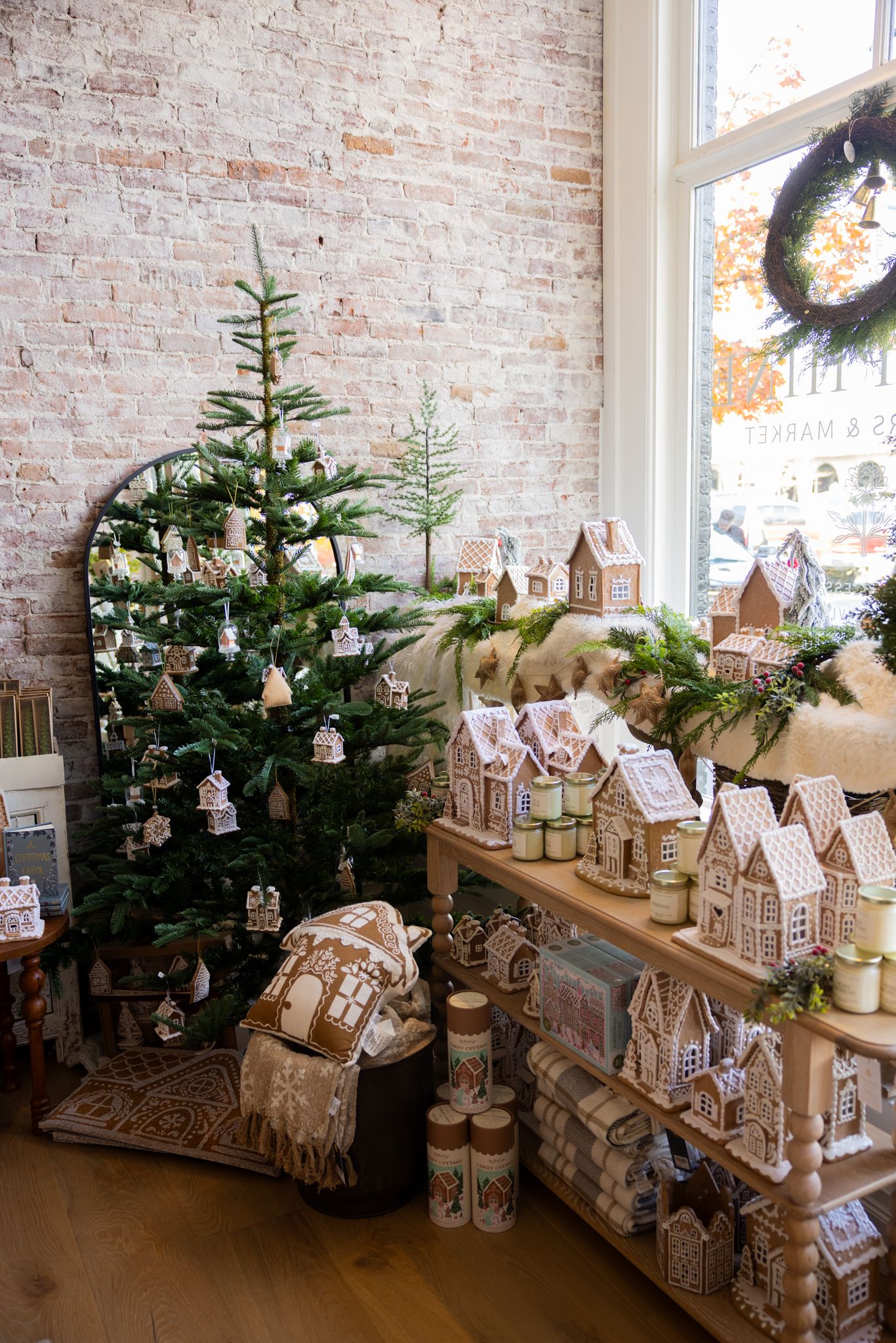 A festive holiday display featuring gingerbread houses and decorated Christmas trees against an exposed brick wall.