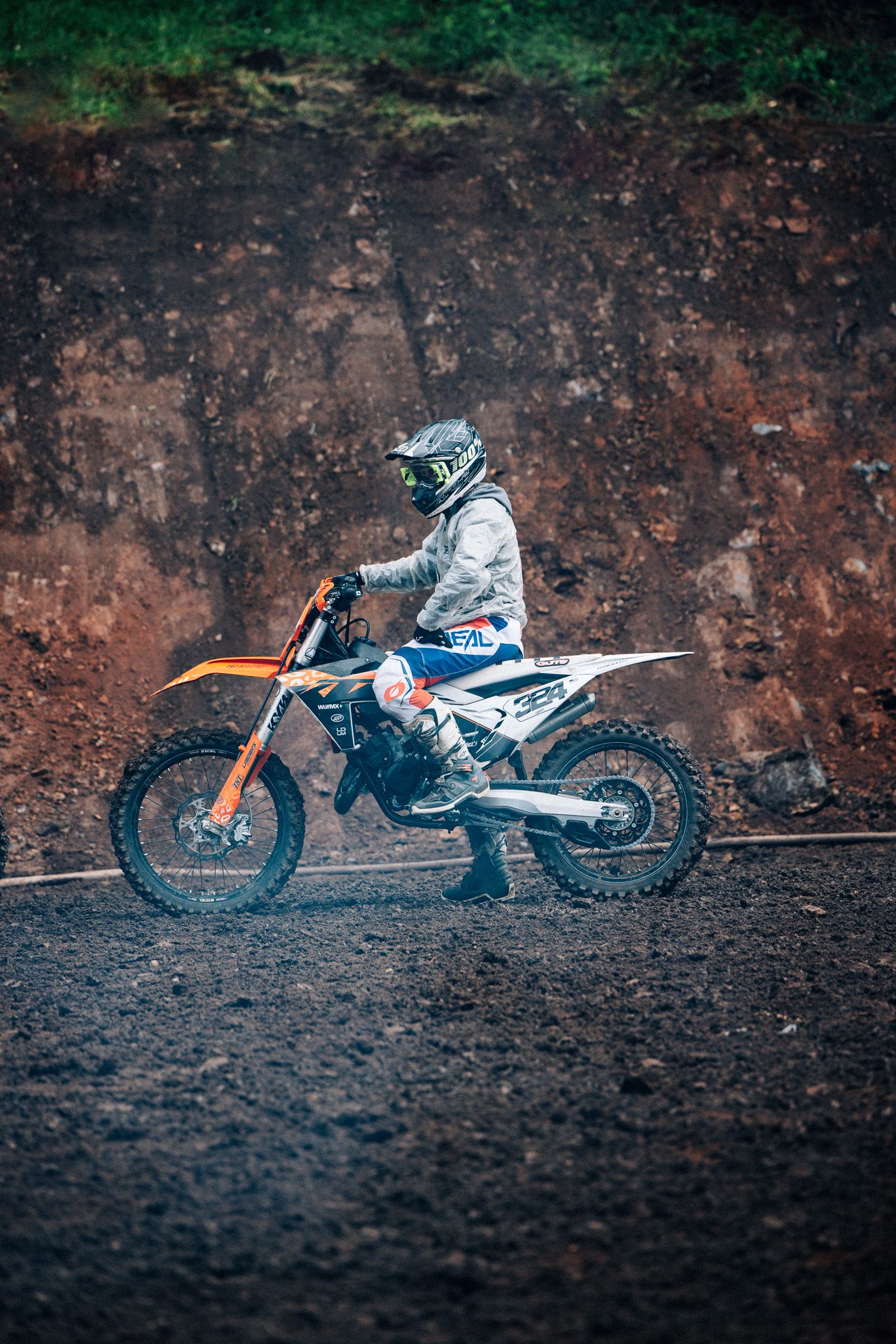 Sequence of orange and white KTM dirt bikes lined up against a dark rocky wall showing progressive side views.