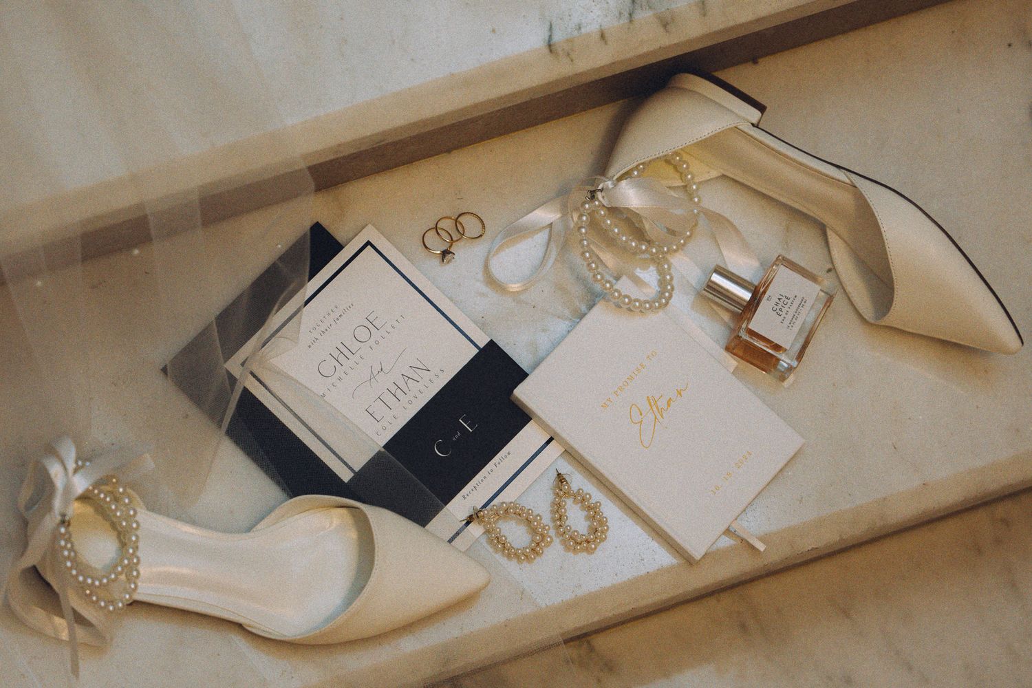 Elegant wedding stationery and accessories arranged on light colored surface.
