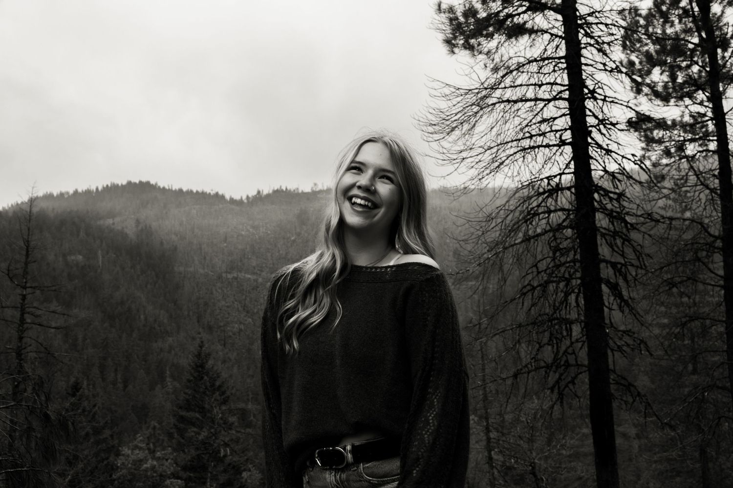 Young woman smiling outdoors in black and white forest mountain landscape photo.