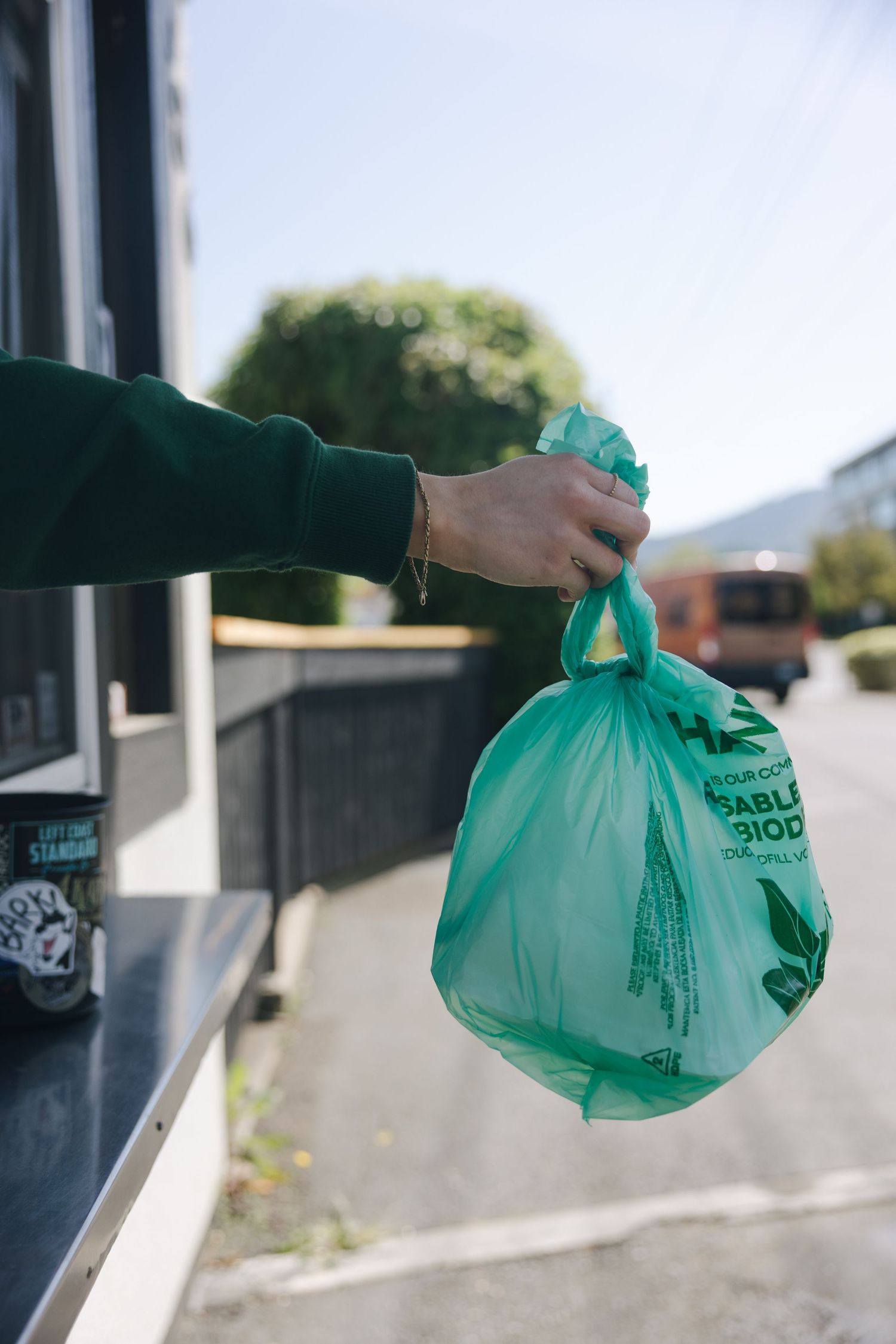 Hand holding a green biodegradable bag outside a building on a sunny day.