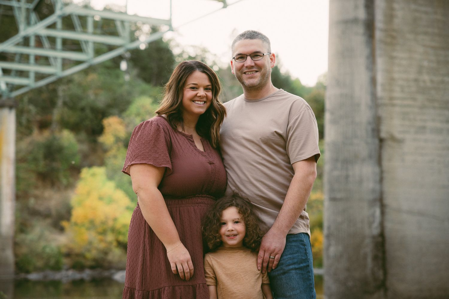A loving family poses together outdoors for a casual photoshoot in earth-toned outfits against a natural backdrop.