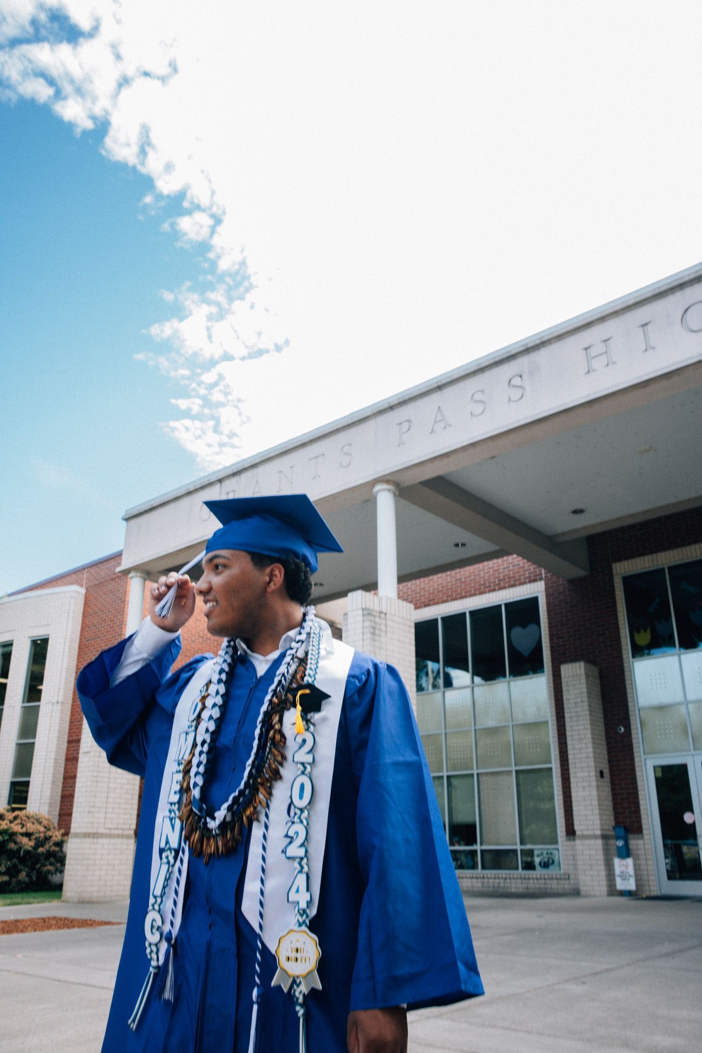 Graduate in royal blue cap and gown poses for photo series outside modern brick and glass building.