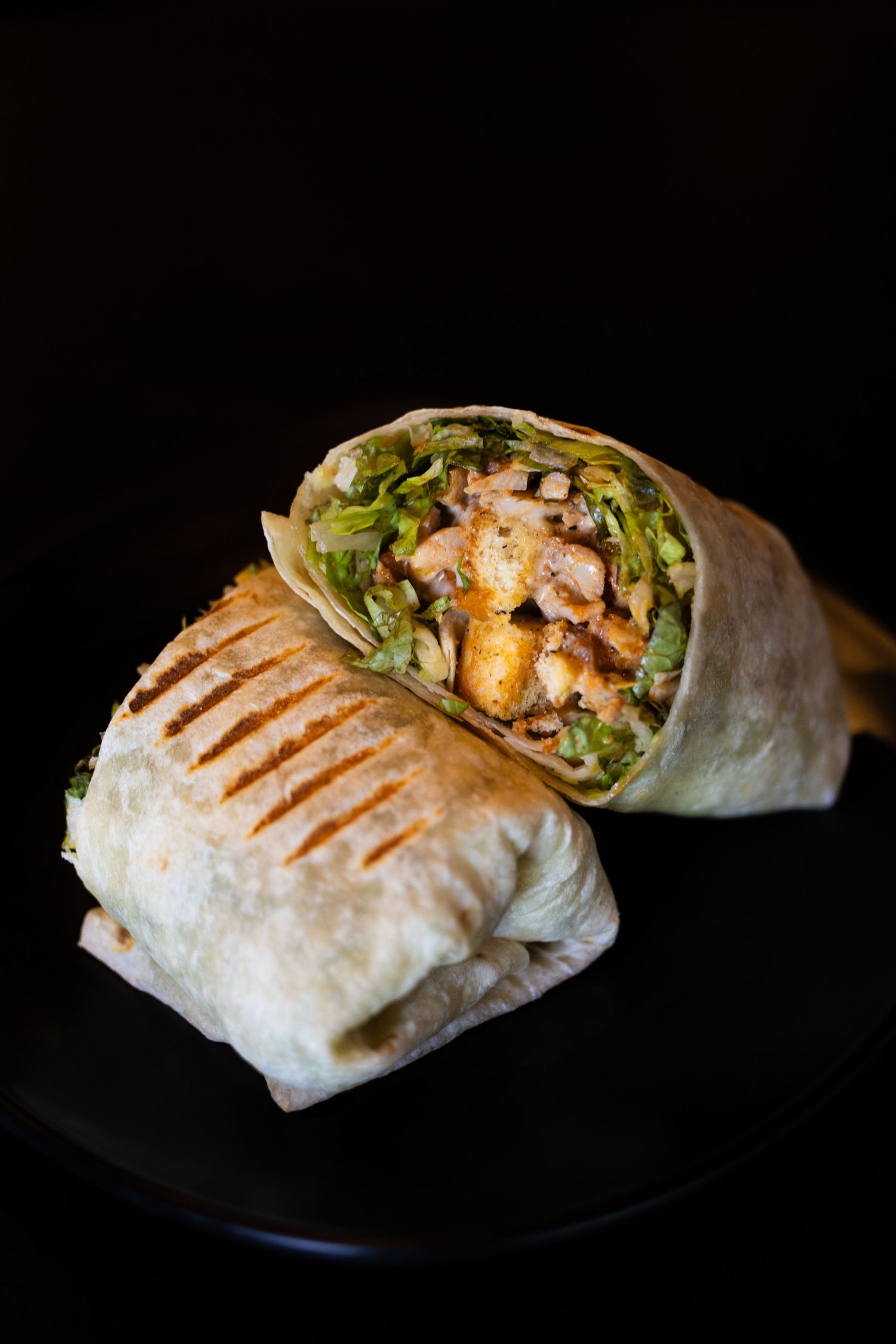 Grilled chicken wrap with fresh lettuce and sauce shown in progression of multiple angles on black plates.