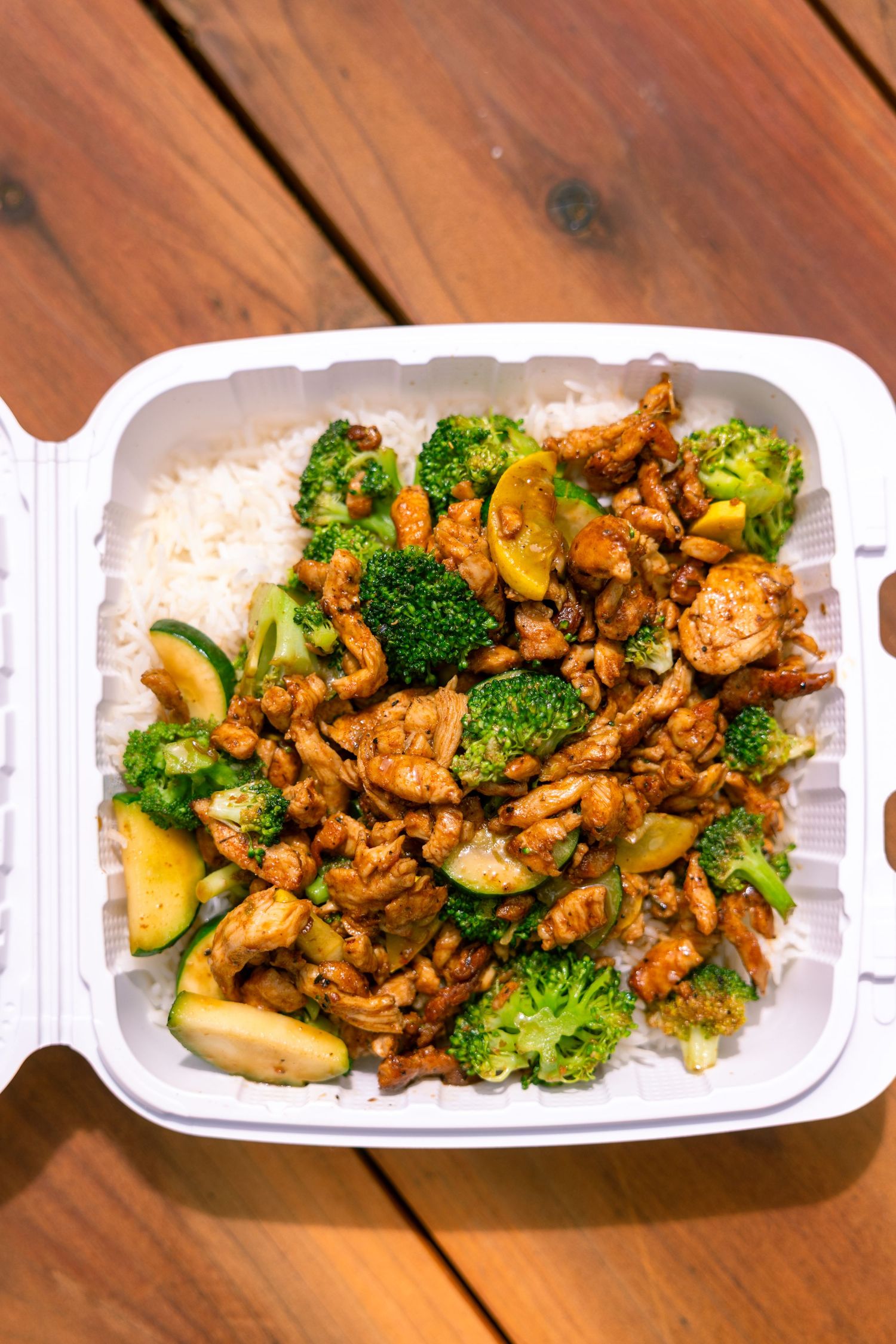 Grilled chicken stir fry with broccoli and zucchini served in white takeout containers on wooden table.