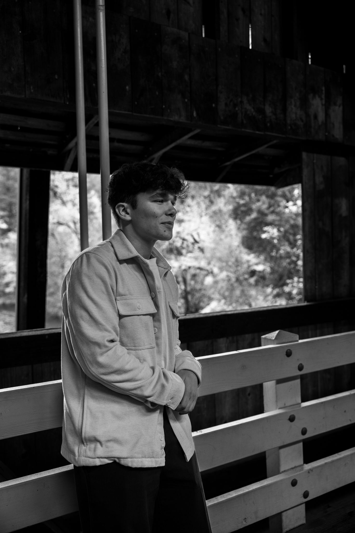 Young man in light jacket stands pensively on a wooden bridge, black and white portrait photography.