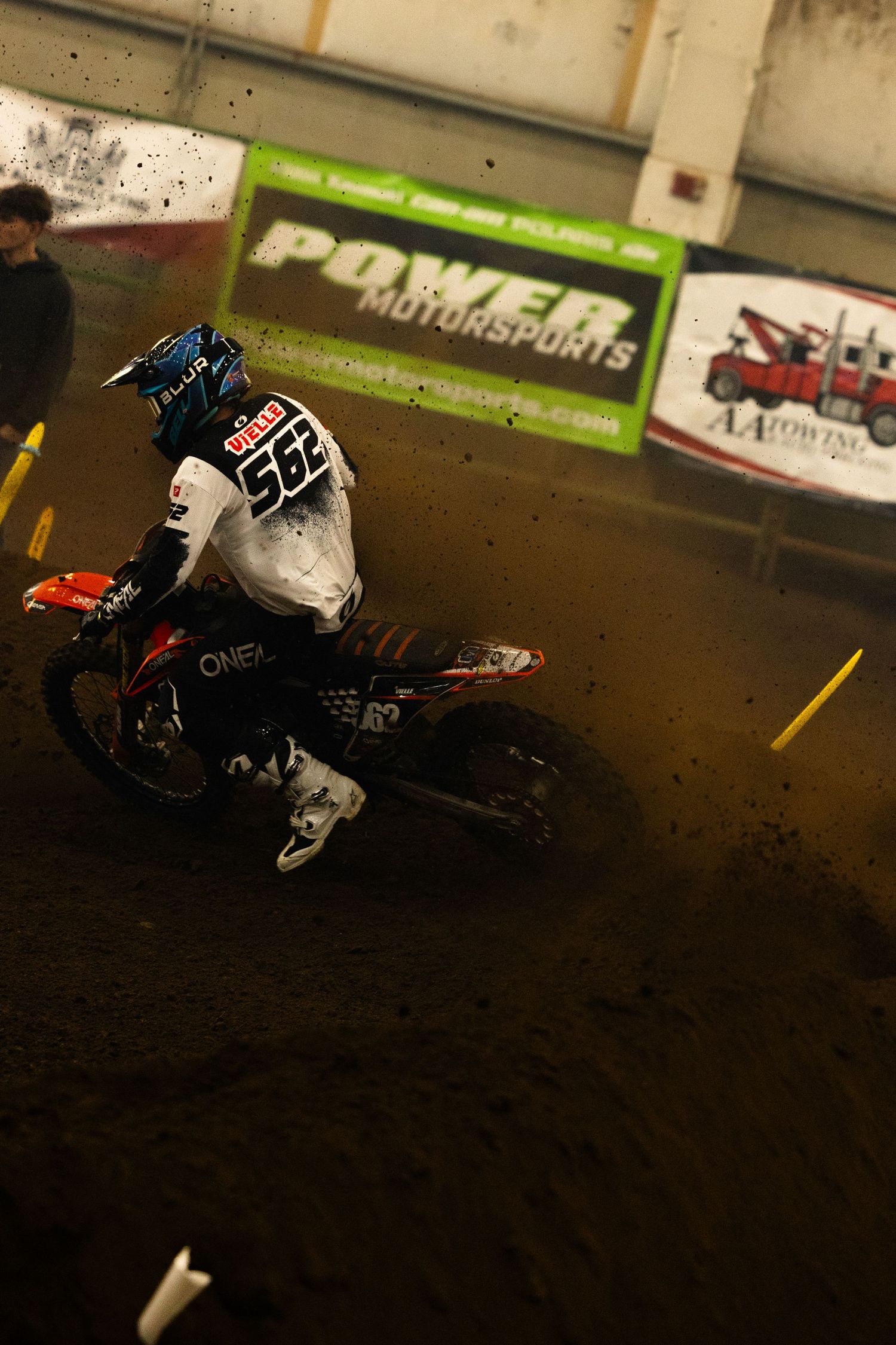 Motocross rider #562 leaning into a dirt turn at an indoor Power Motorsports racing event.