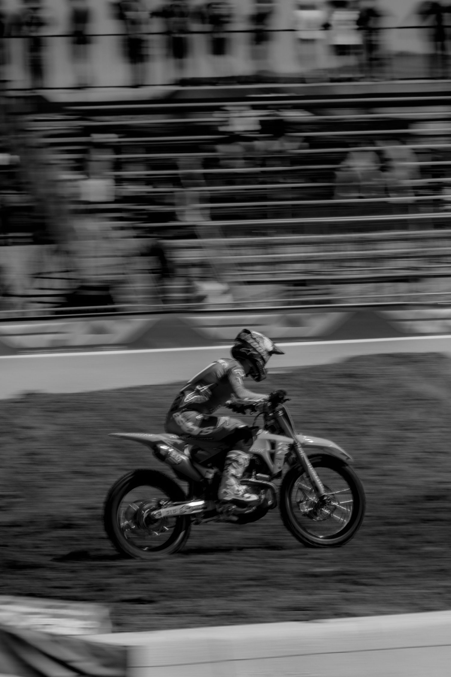 A black and white motion-blurred sequence of a motorcycle racer leaning into a turn on a racetrack.