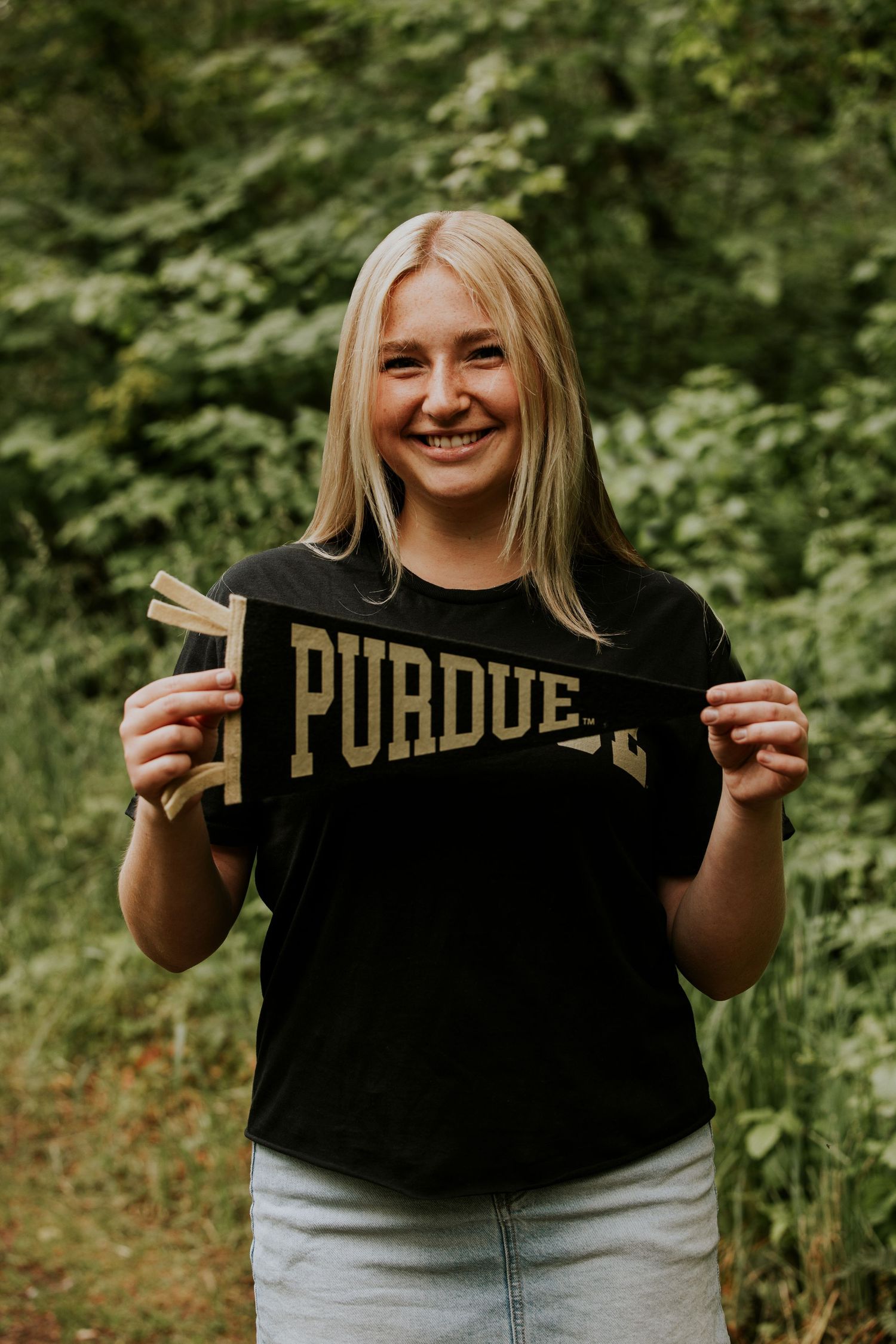 Someone in a black Purdue t-shirt holds up a vintage university pennant while standing outdoors.