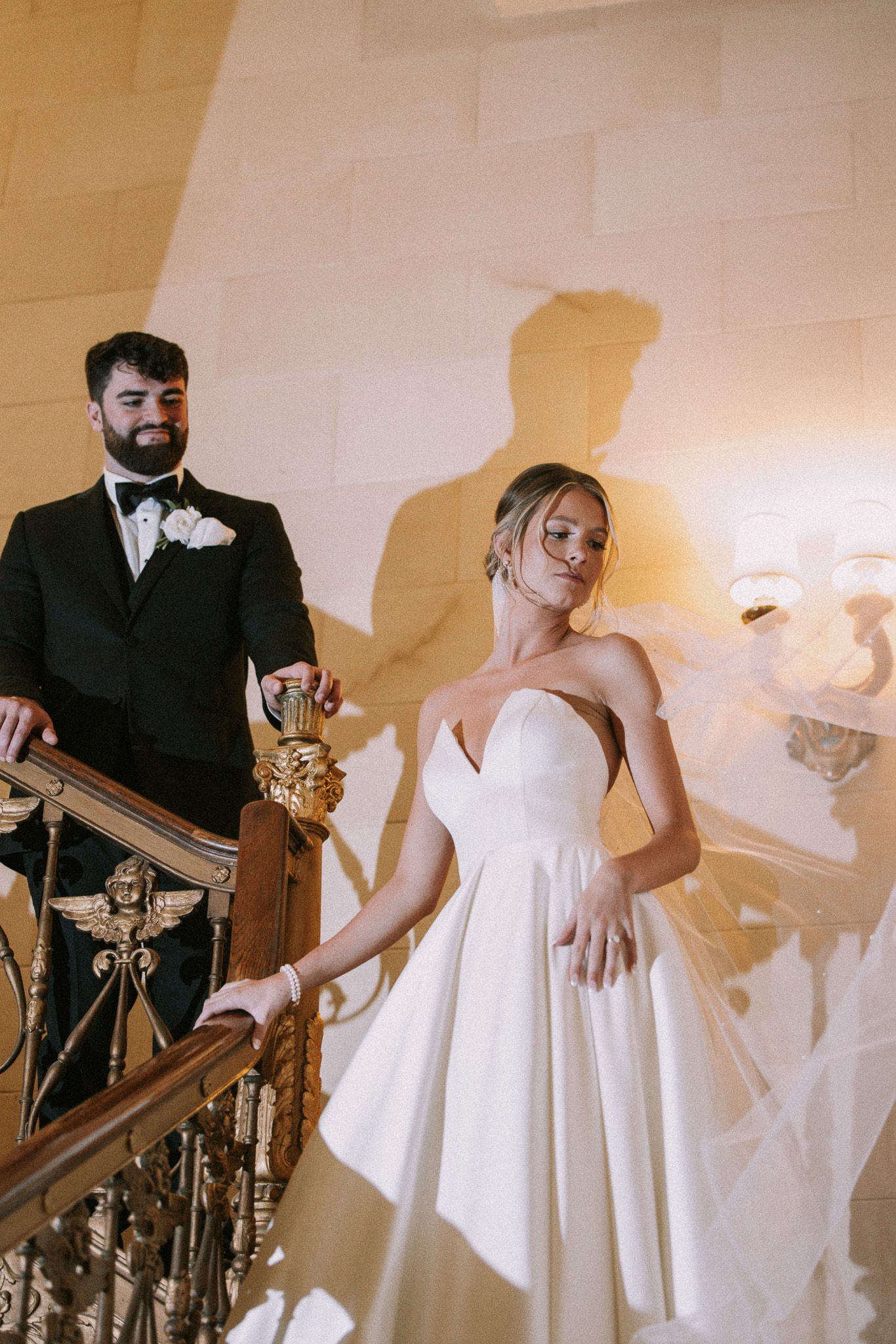 Wedding party in formal attire ascending elegant staircase with ornate railing.