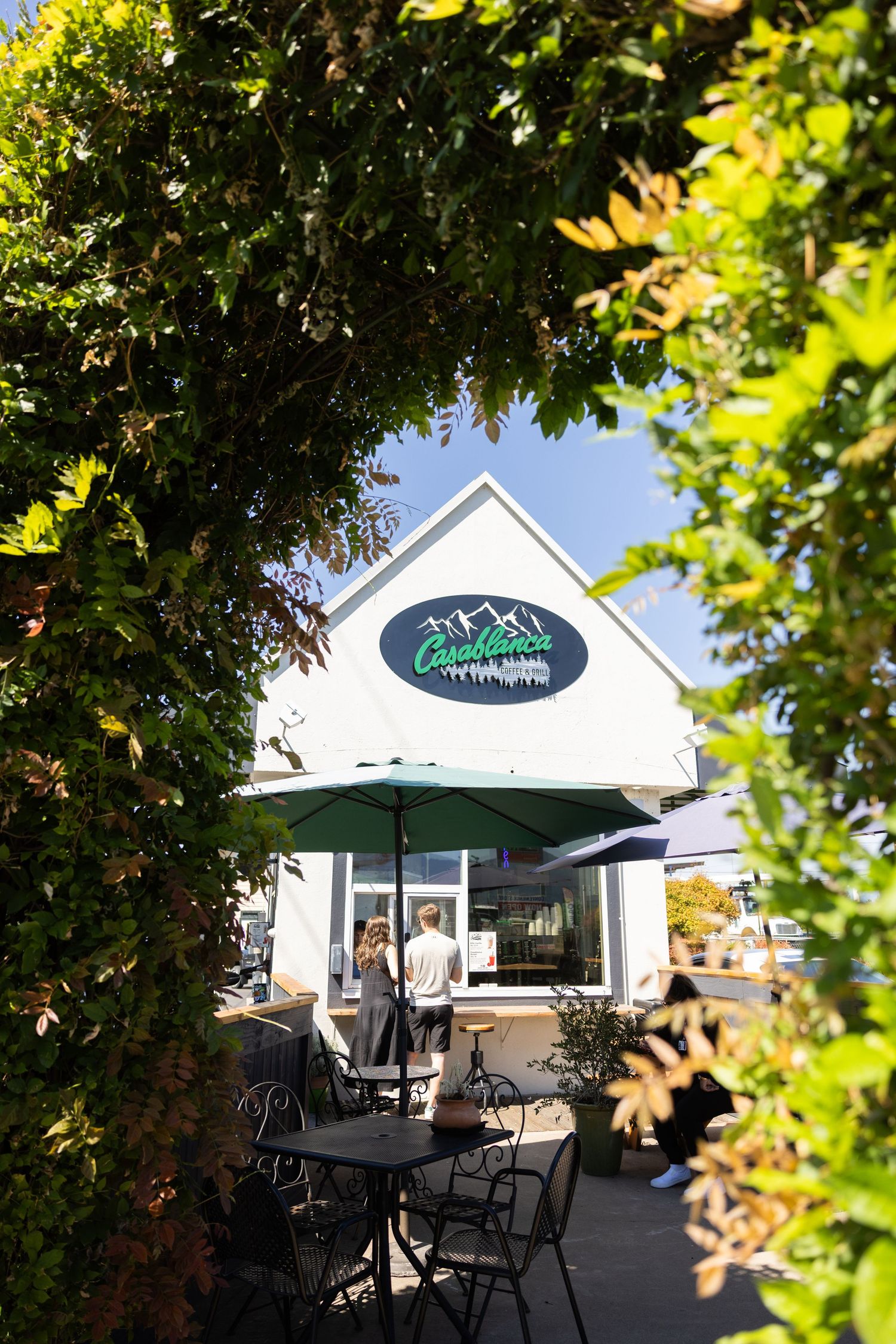 A series of outdoor patio views at a bistro with umbrella-shaded tables and white building exterior framed by green foliage.