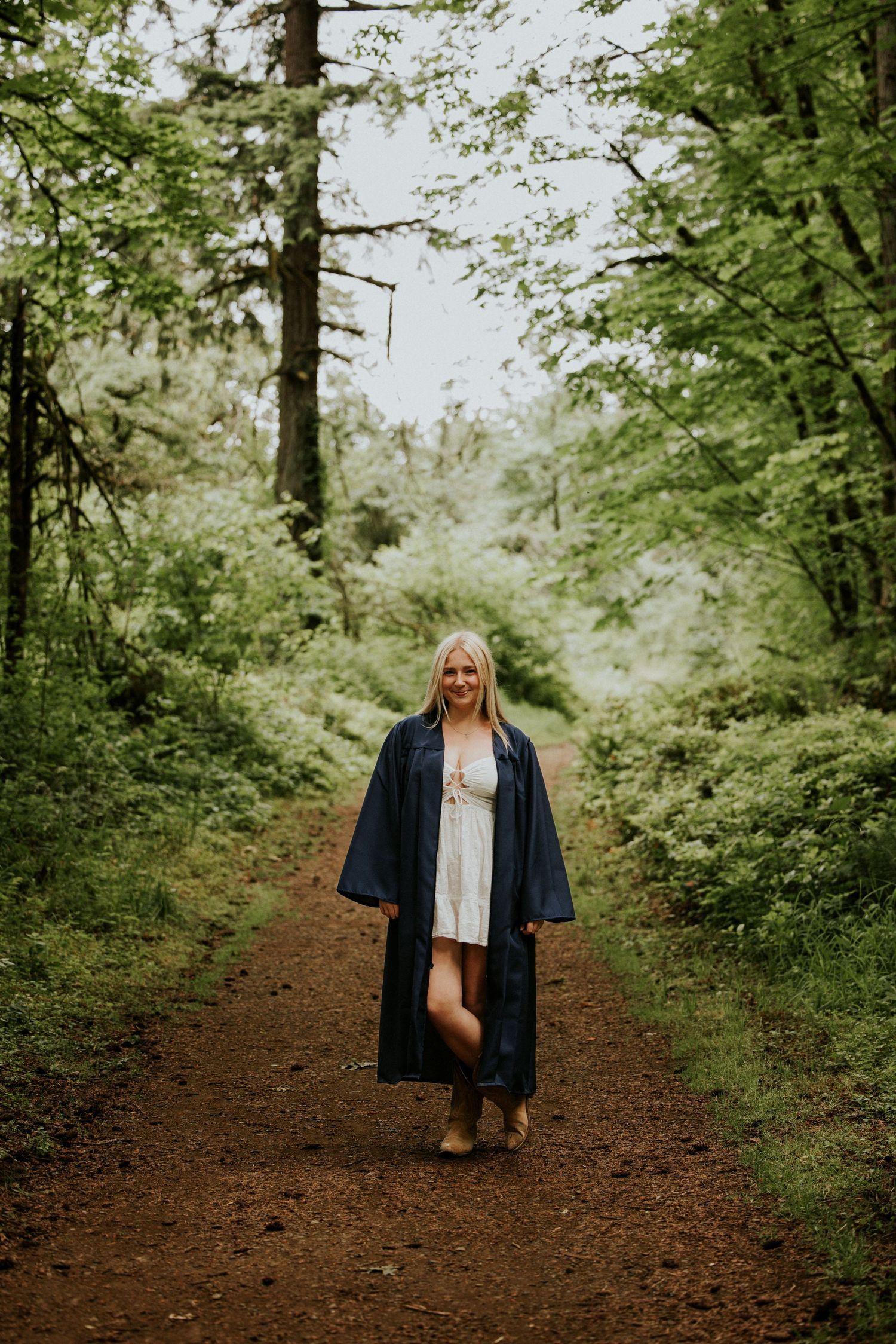 A person in a blue jacket walks along a scenic dirt trail through a lush green forest.