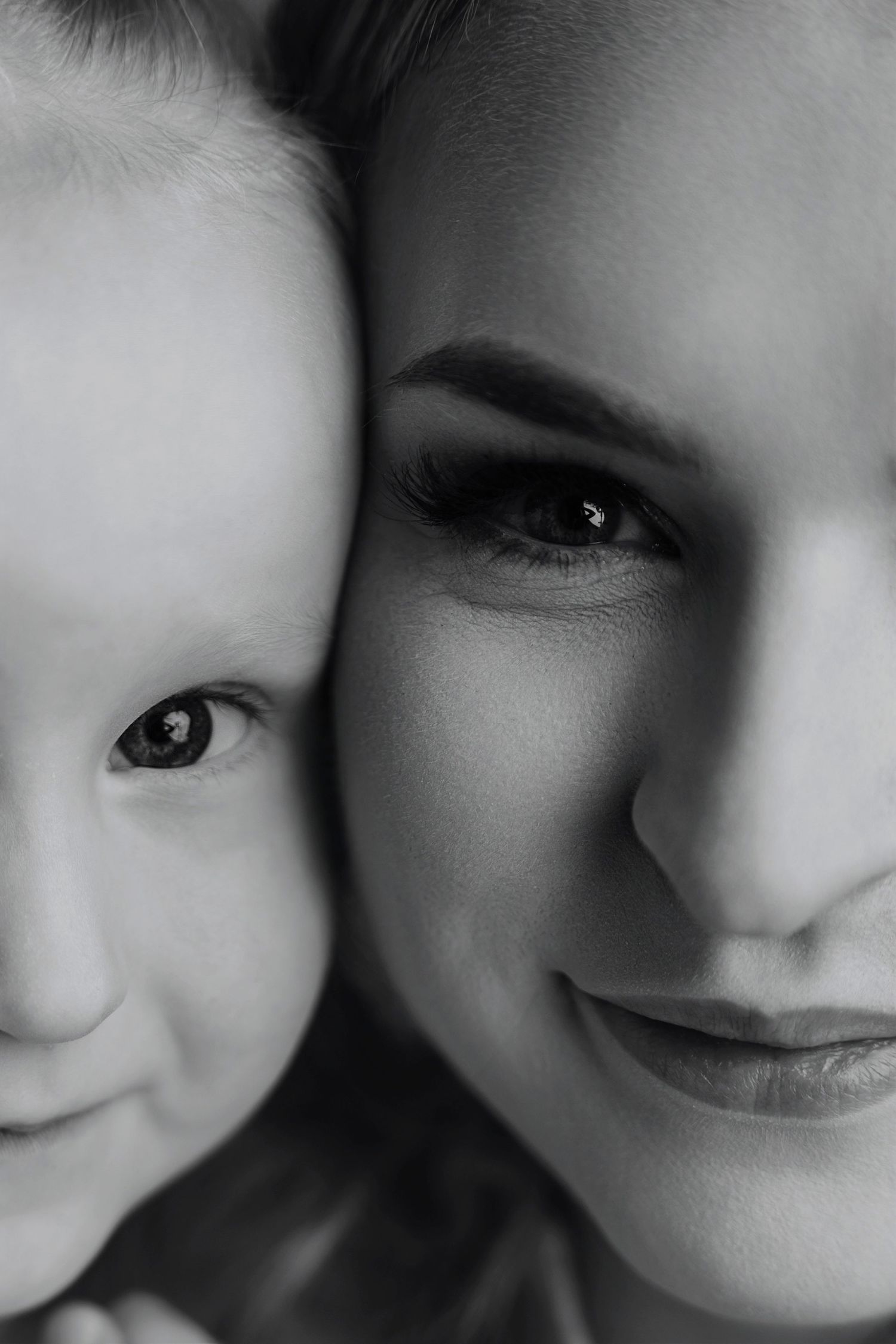 Black and white close-up portrait of a mother and baby cheek to cheek, smiling warmly.