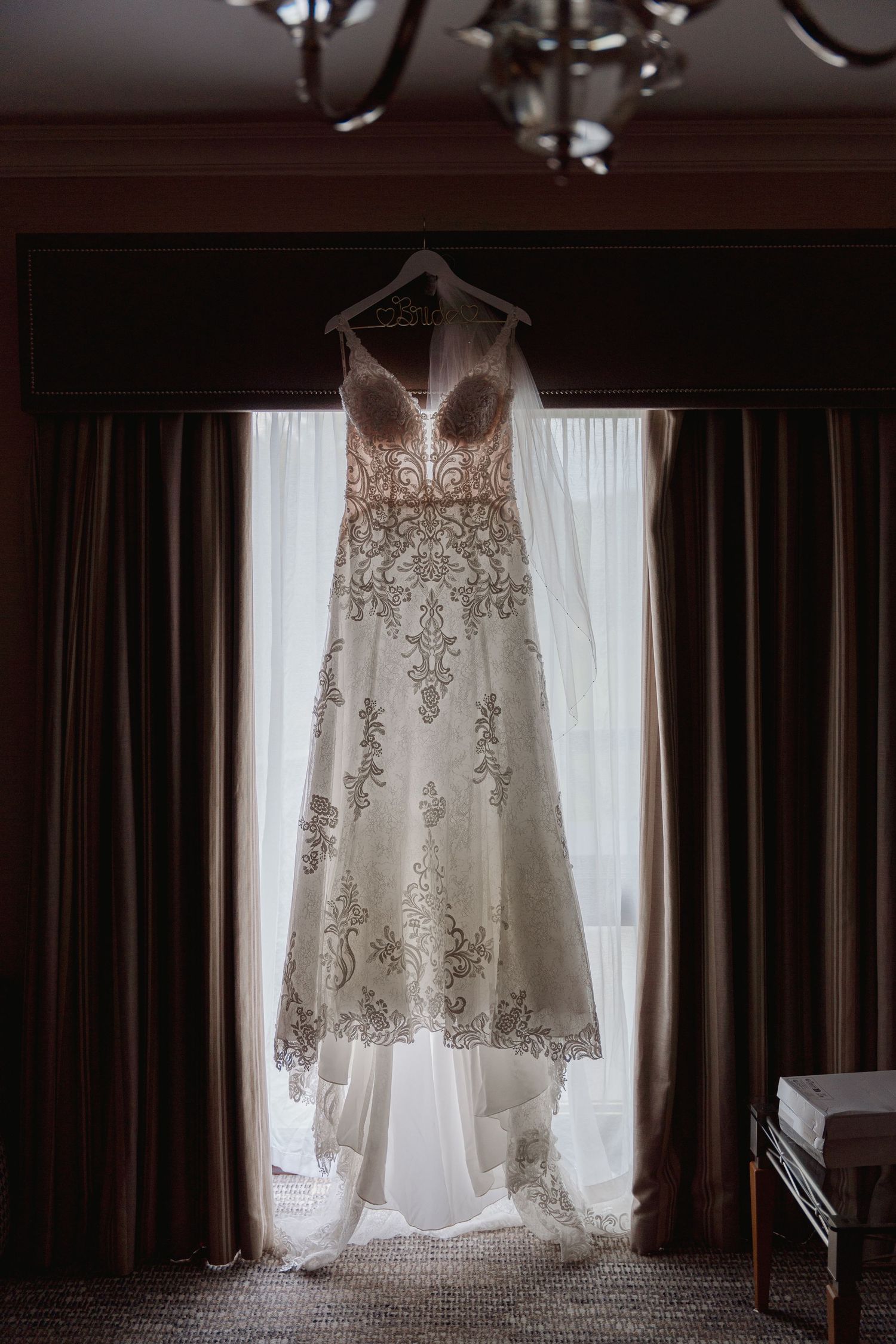 Elegant lace wedding dress hanging in window light before the ceremony.