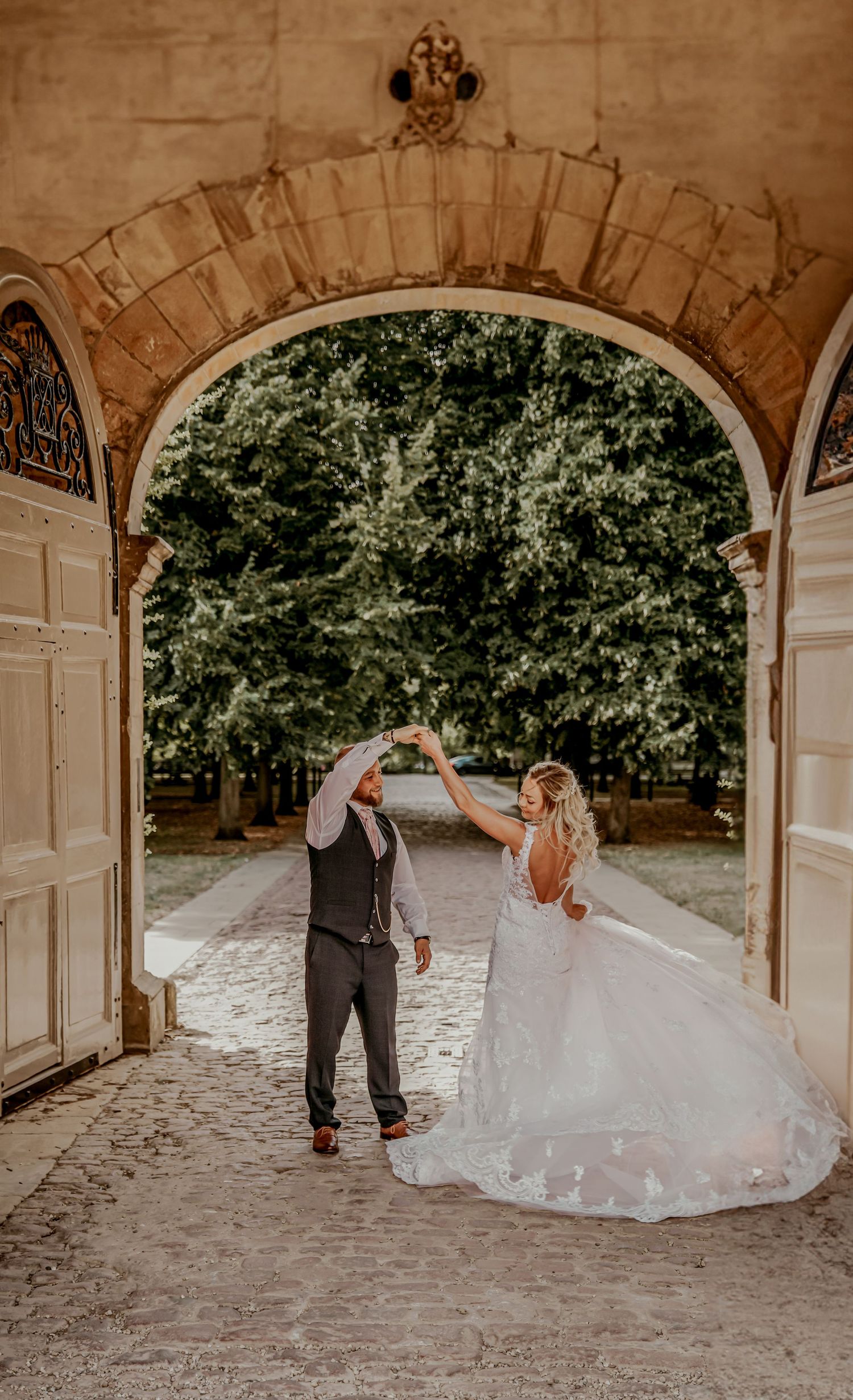 Newlyweds share a romantic dance under an elegant stone arch surrounded by greenery on their wedding day.