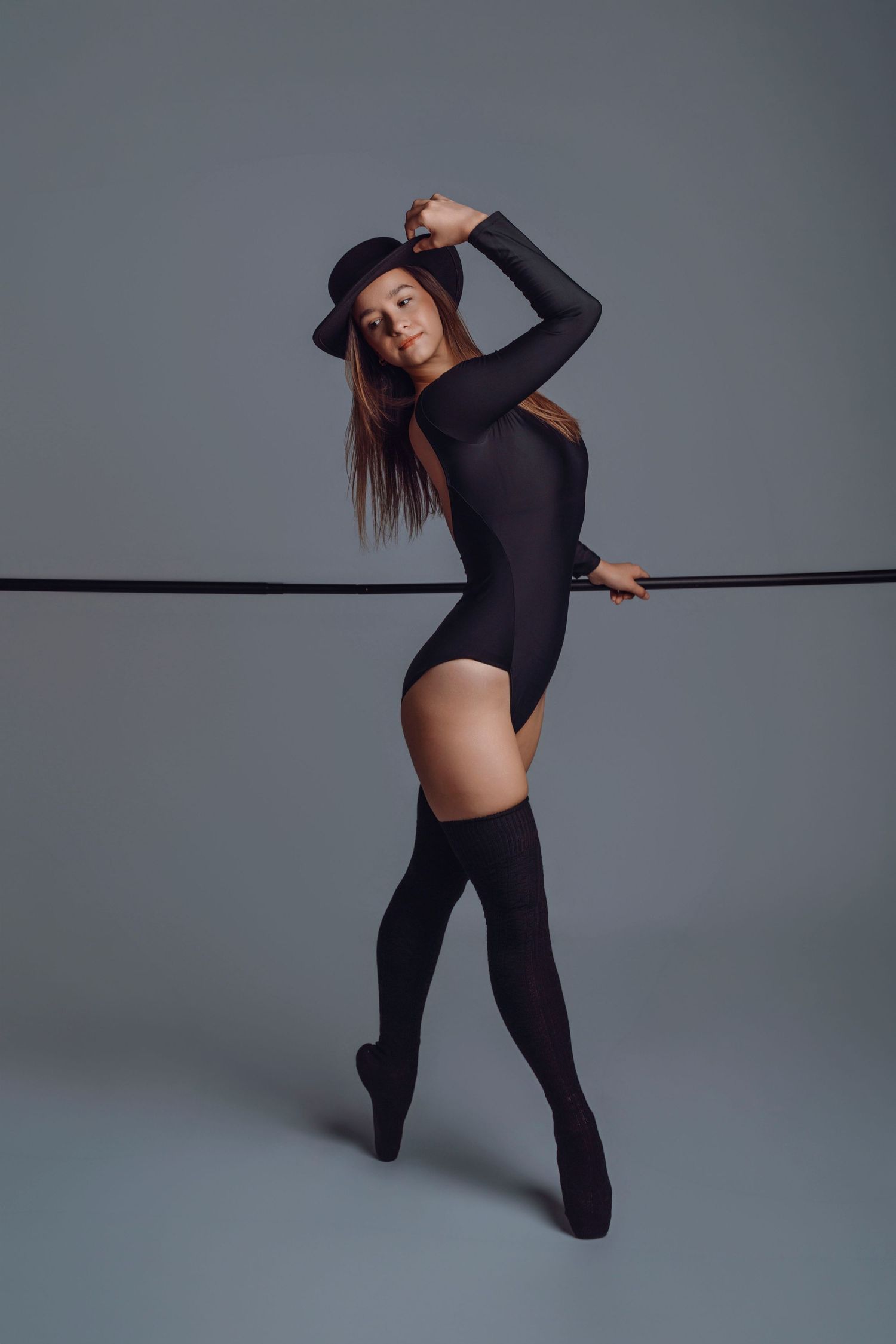 A dancer in a black bodysuit, hat, and thigh-high socks poses gracefully with a rope in a studio.
