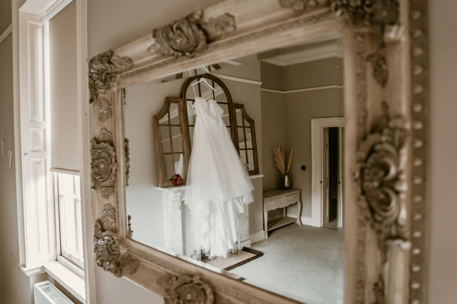 Wedding dress reflected in ornate vintage gold mirror in bright elegant dressing room.