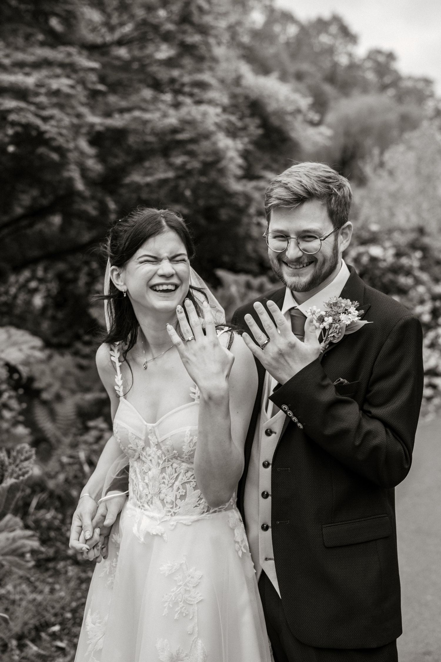 Newlyweds joyfully show off their wedding rings to the camera in a charming black and white photo.