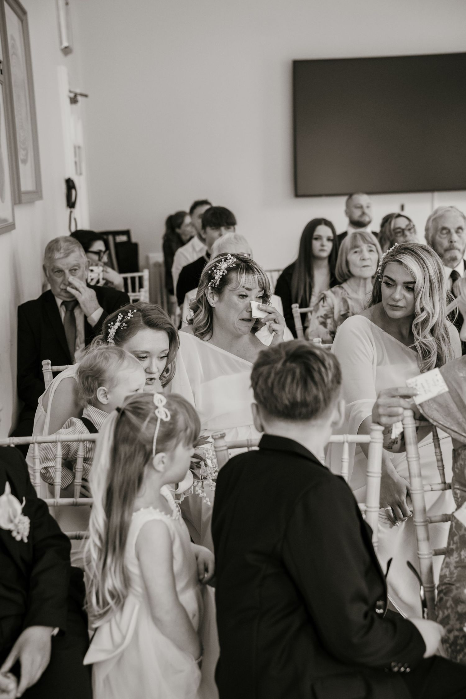 Emotional wedding guests including bride wiping tears during heartfelt ceremony in black and white.