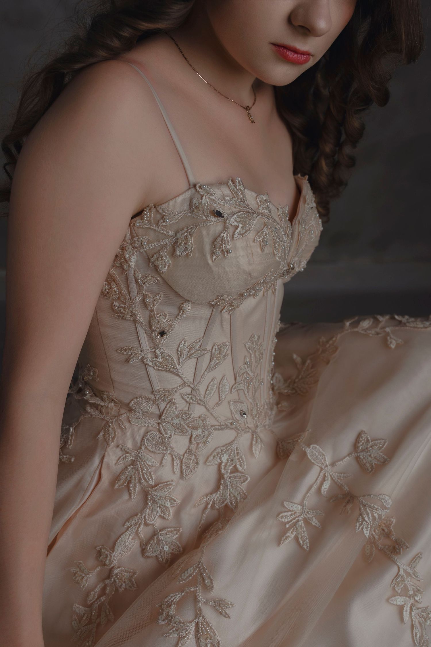 Woman in elegant champagne floral embroidered corset gown with delicate lace detailing and spaghetti straps.