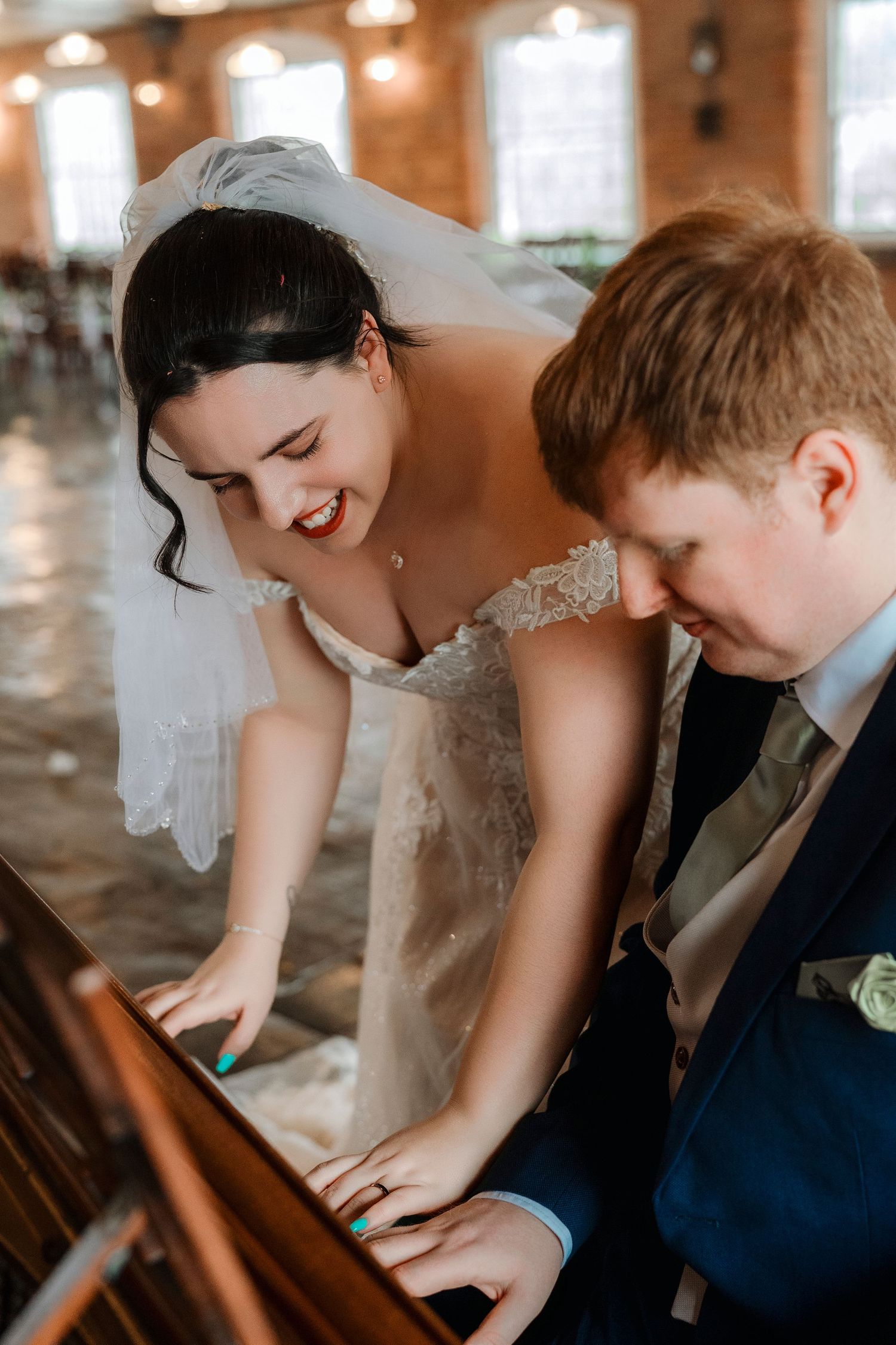 Bride and groom laughing together while playing a vintage piano at their wedding reception.