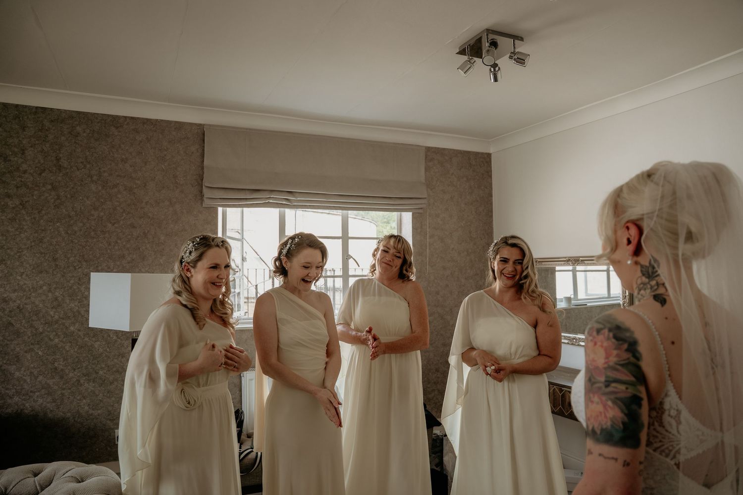 Bride with tattoos showing bridesmaids in white dresses her wedding look.