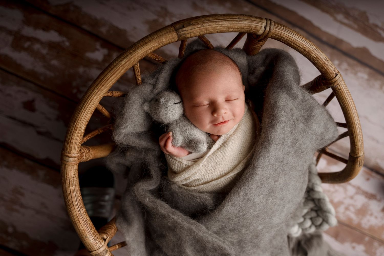 Peaceful sleeping newborn swaddled in gray wrap with a small stuffed bunny inside a round wicker basket.
