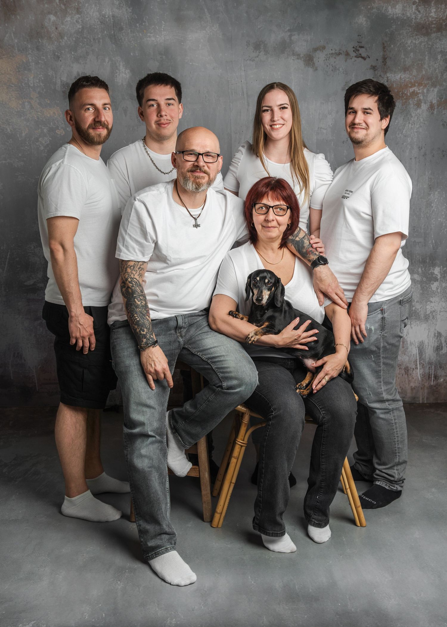 Family of five in white shirts poses with a black dachshund for a studio portrait photo.