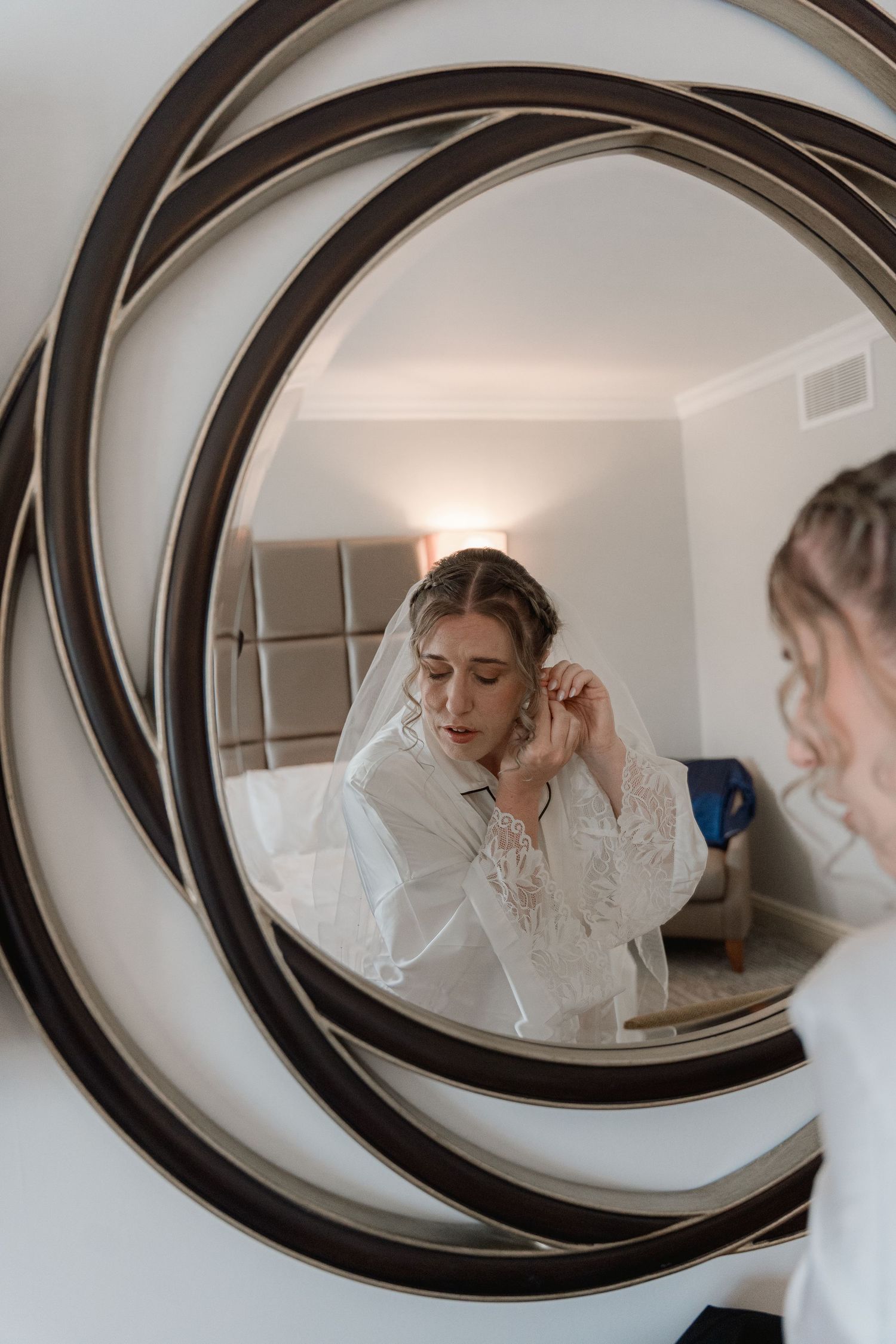 Bride adjusting veil reflected in unique circular spiral mirror while getting ready.