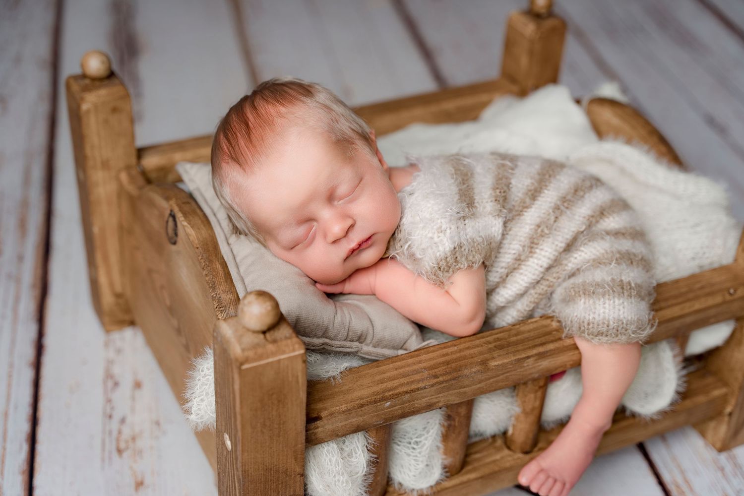 Sleeping newborn baby in striped knit romper resting peacefully in a rustic wooden mini bed.