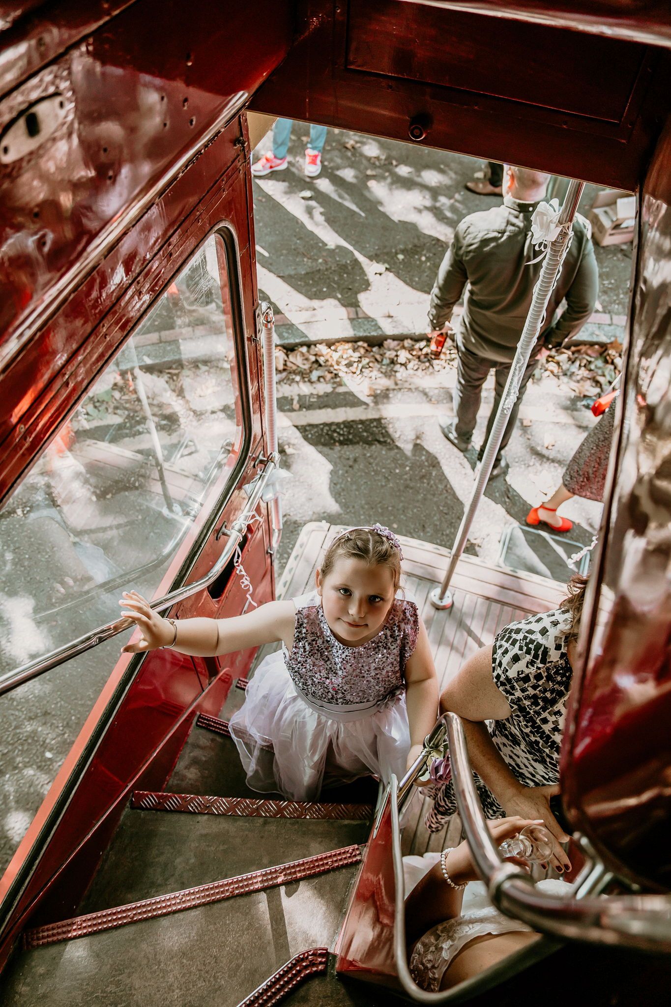 Young flower girl in white dress climbing stairs inside vintage red double-decker bus.