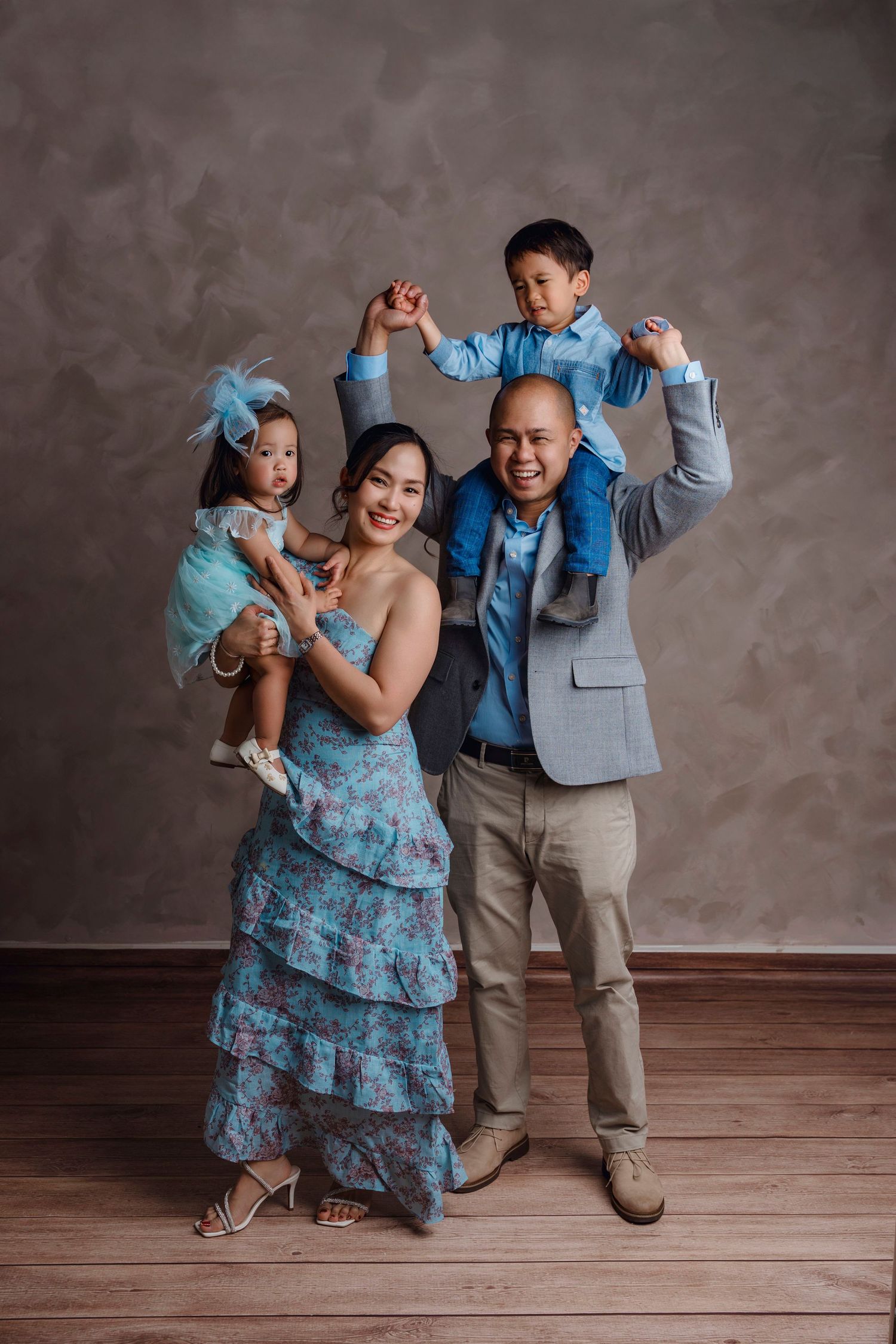 Happy Asian family in blue outfits posing in studio, parents with two young children smiling together.