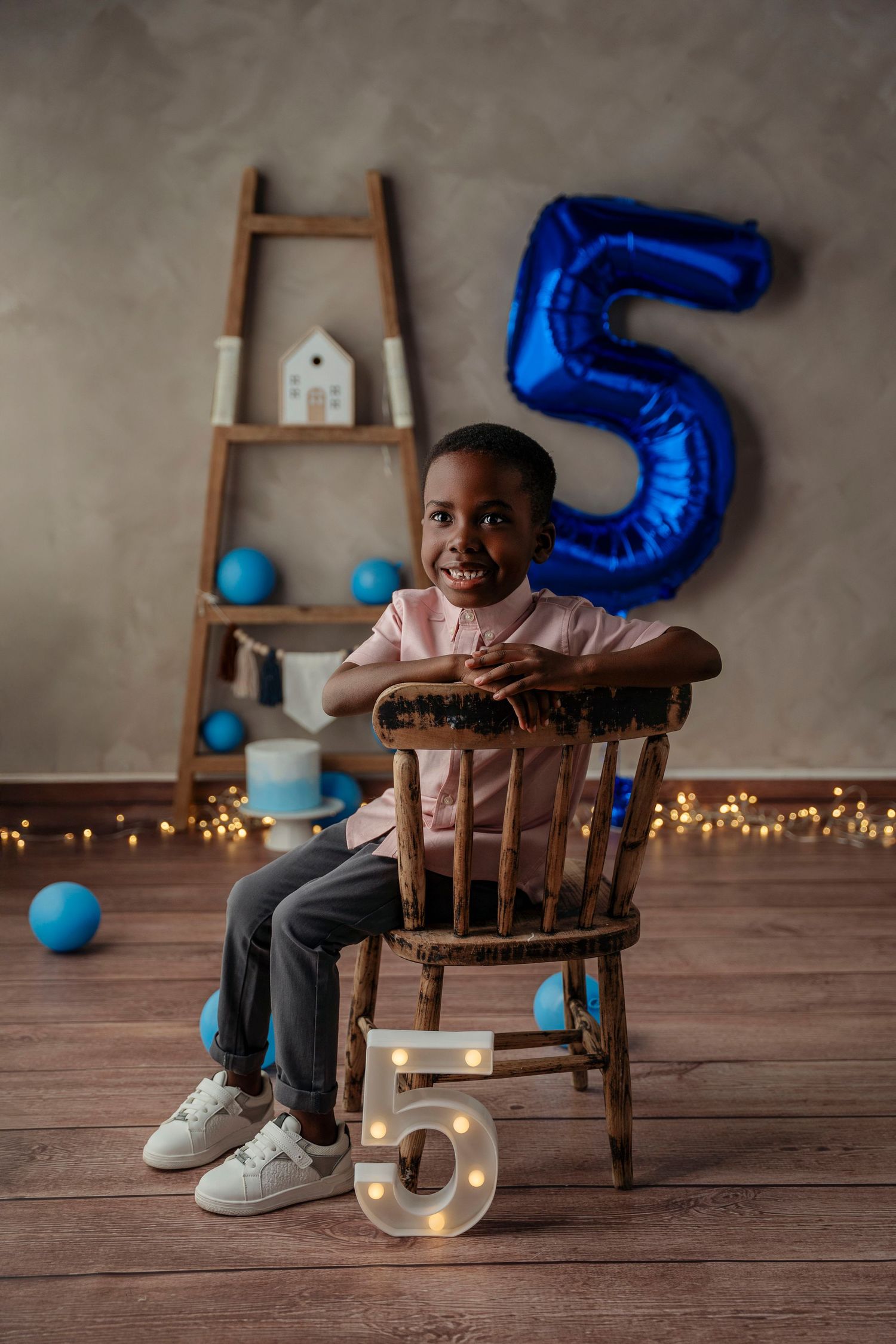 Smiling boy sitting on wooden chair at 5th birthday party.