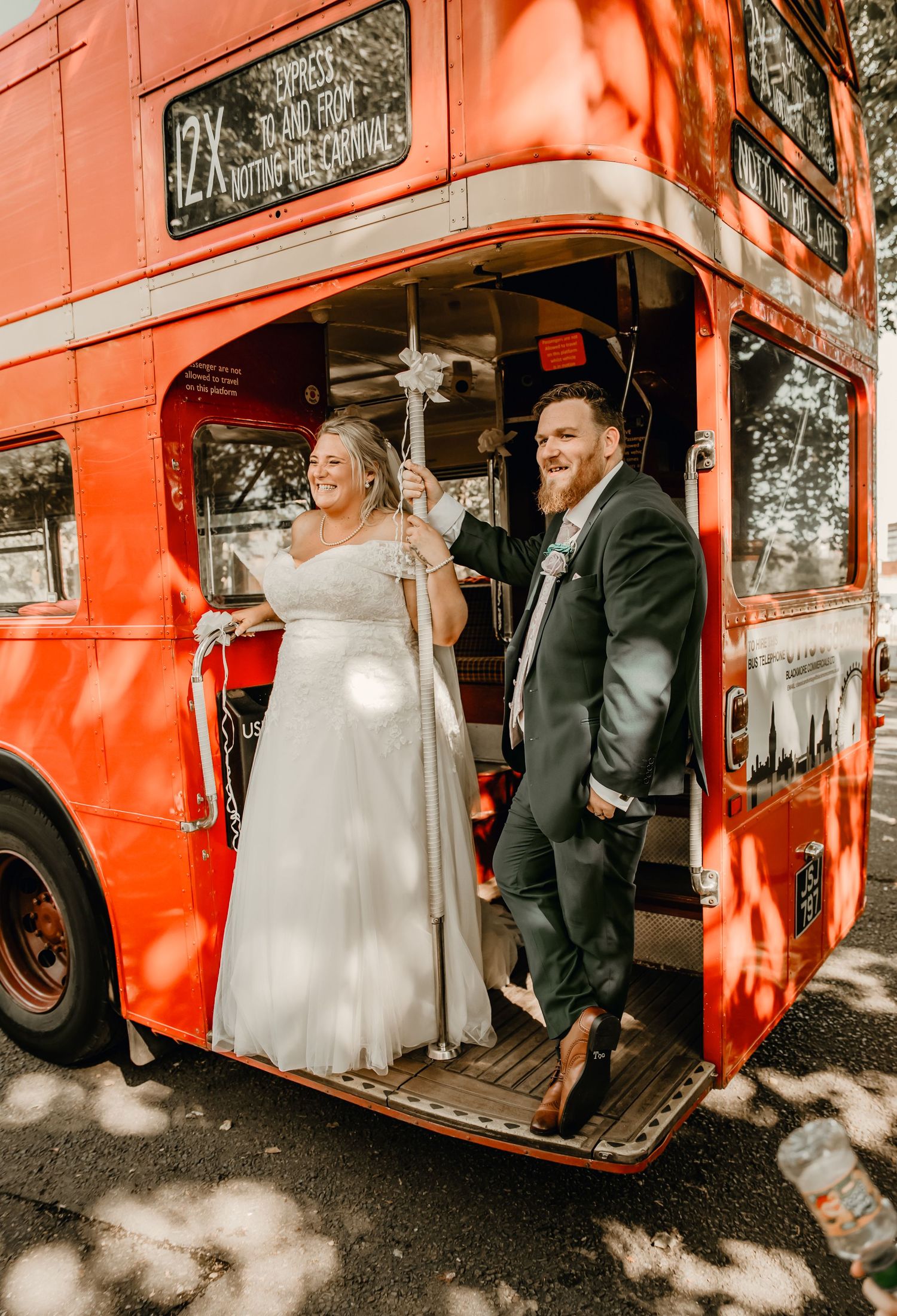 Smiling bride and groom pose on iconic red London double-decker bus on their wedding day.