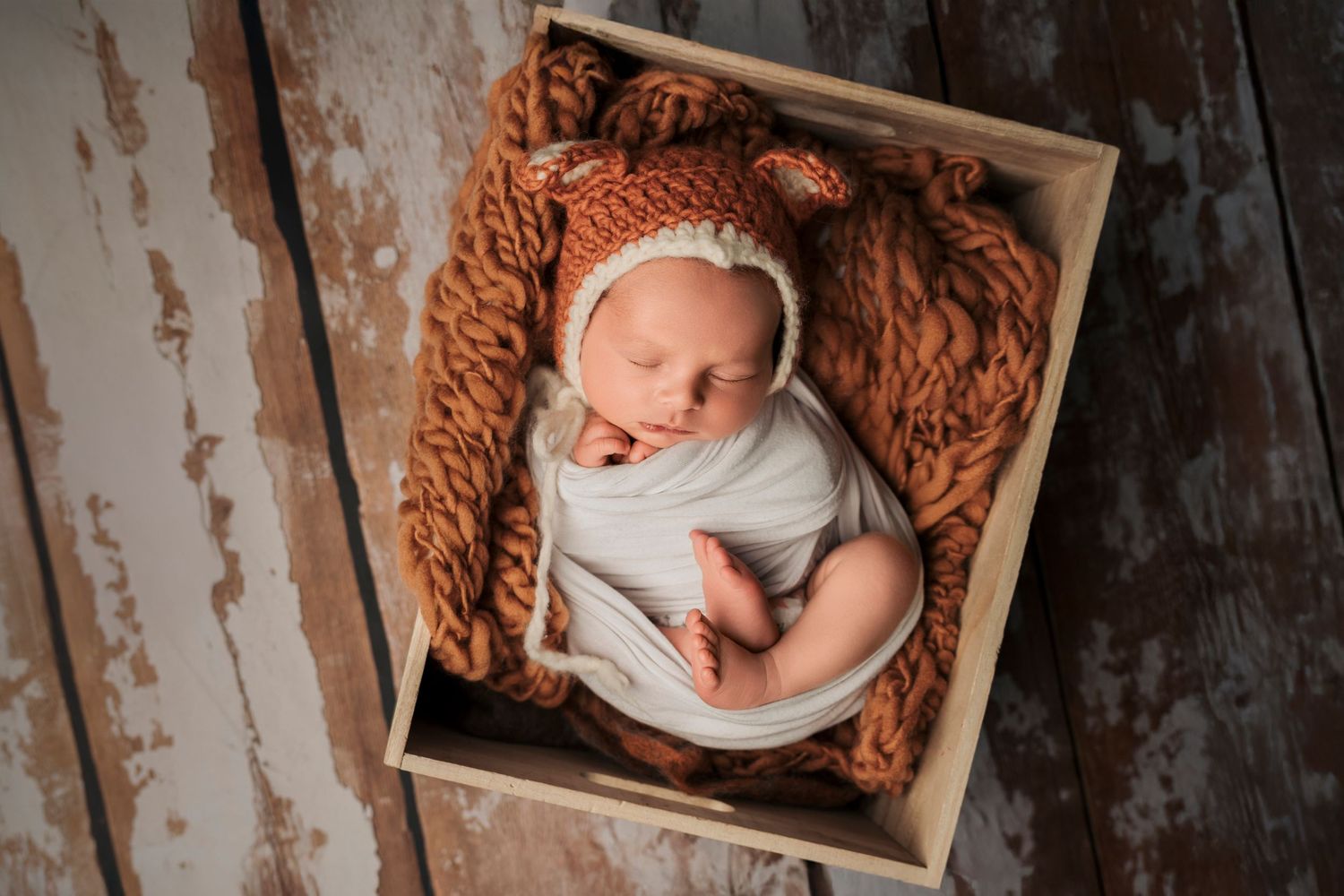 Newborn baby sleeping in a wooden box with a brown fuzzy bear bonnet and wrap.