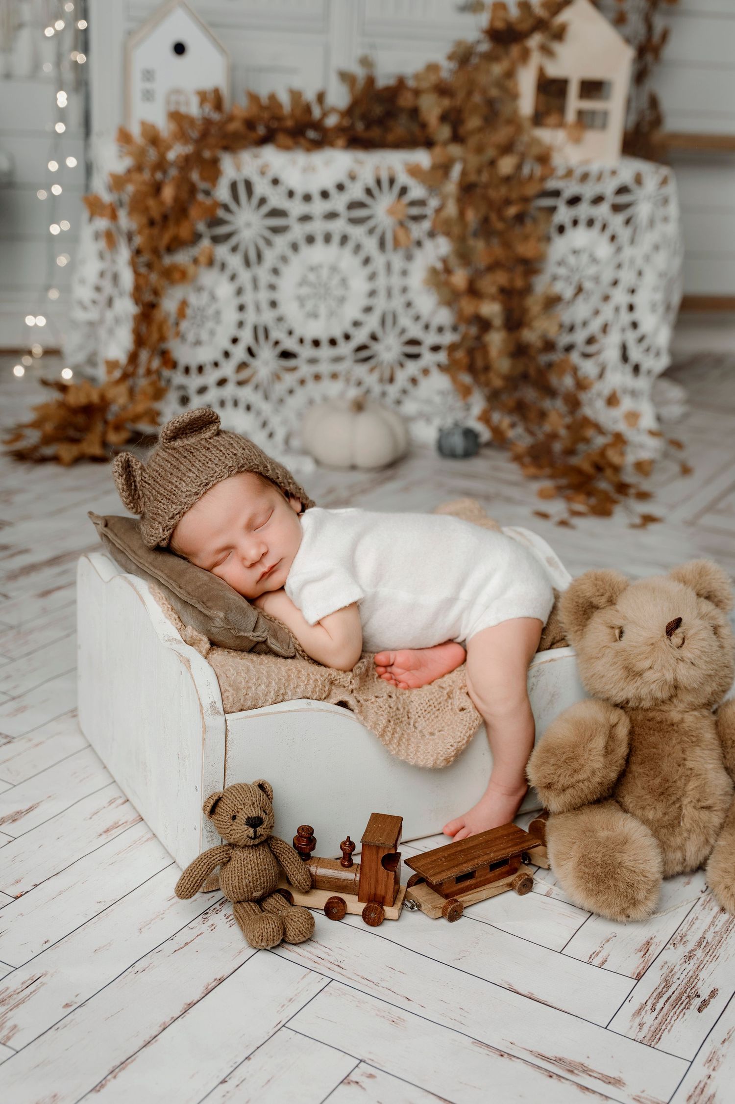 Newborn baby in bear hat sleeping on tiny bed surrounded by teddy bears and toys.