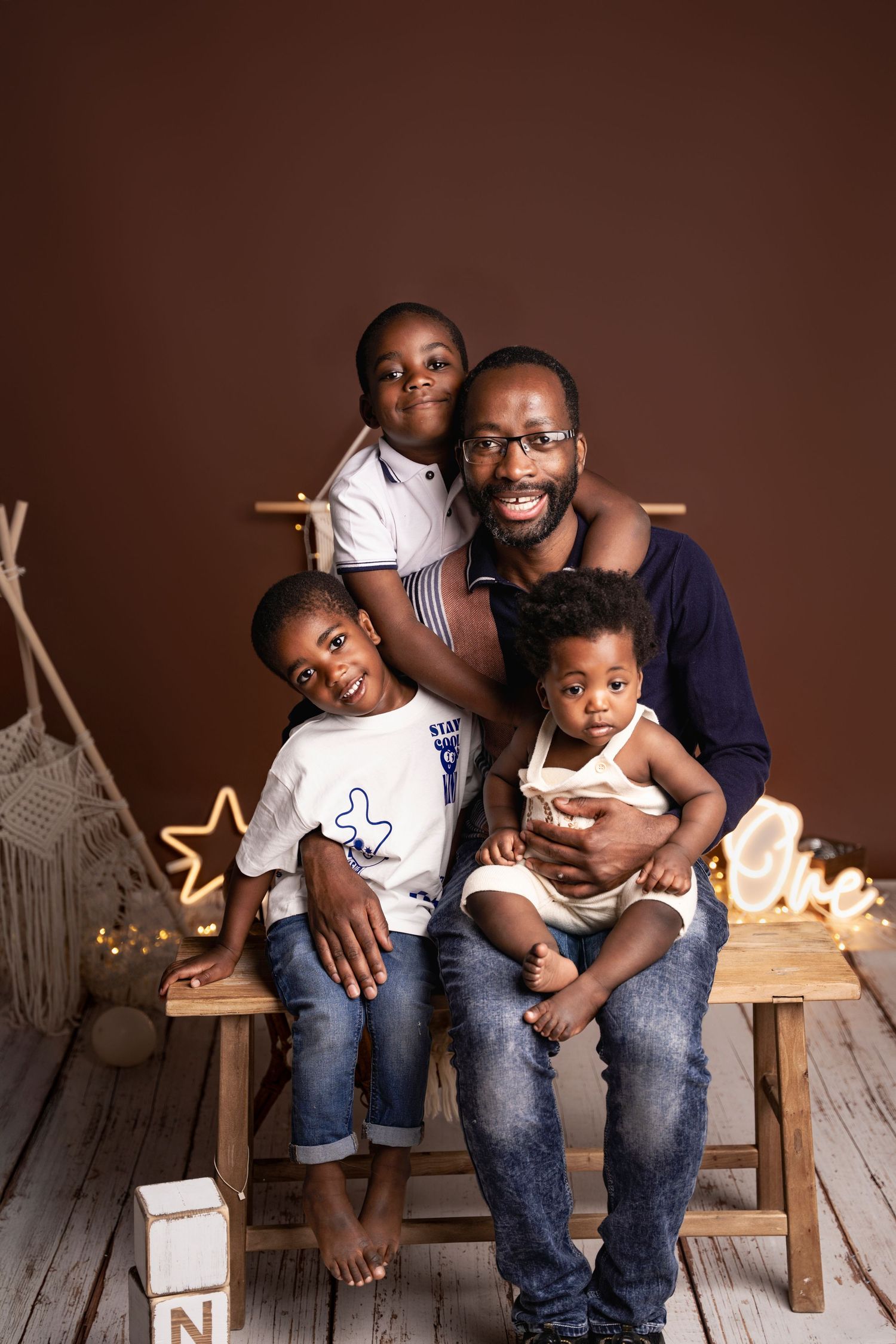 A joyful father poses with his three young children in a warm studio portrait with festive star decorations.