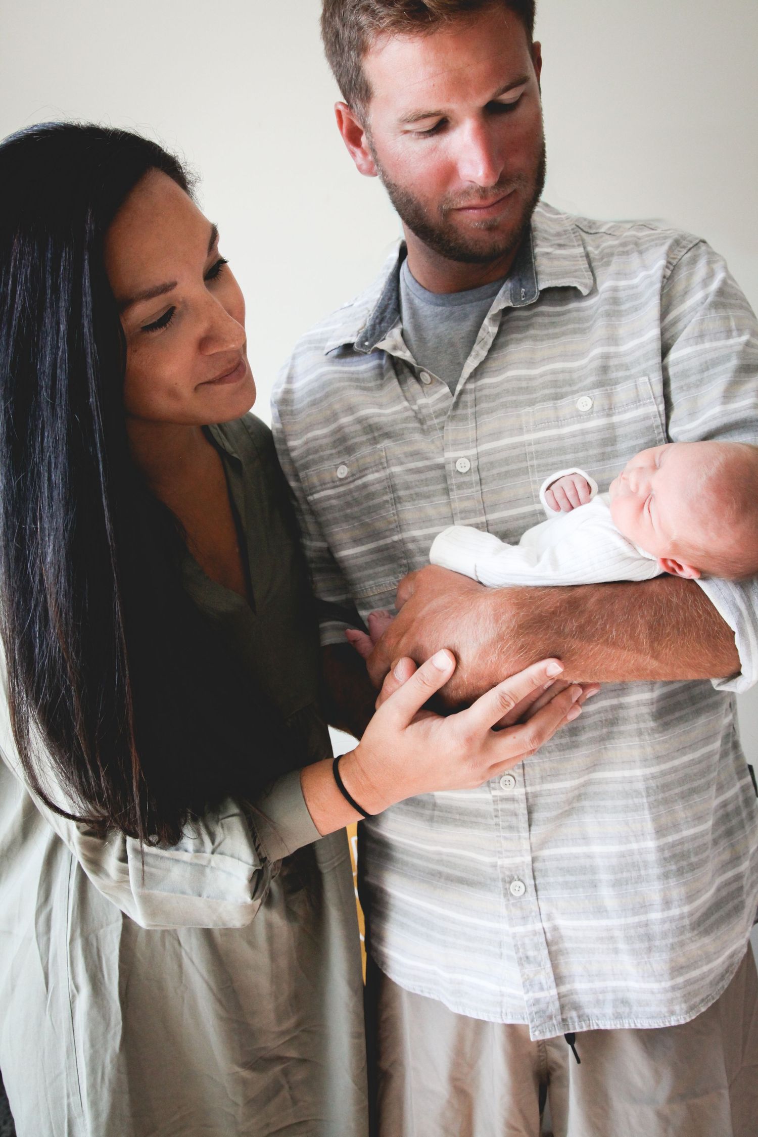 Series of intimate lifestyle photos showing couple with newborn against white wall background.
